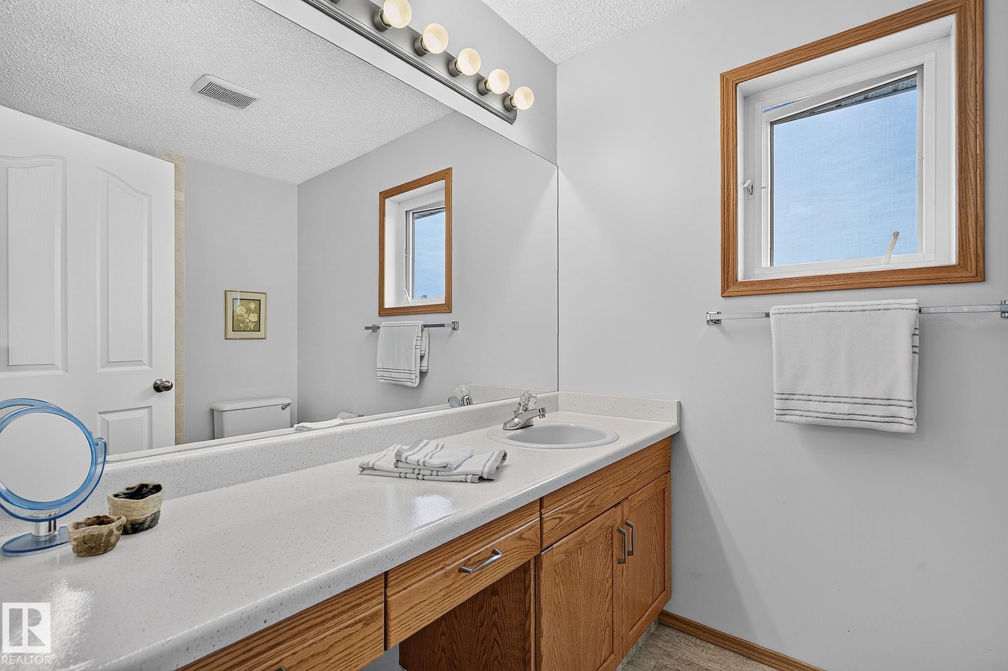 Bathroom vanity in the ensuite featuring a long countertop with an integrated sink, light wood-finish cabinetry, and a full-width mirror - 385 Meadowview Terrace, Sherwood Park, AB - Indoor Photo Showing Bathroom