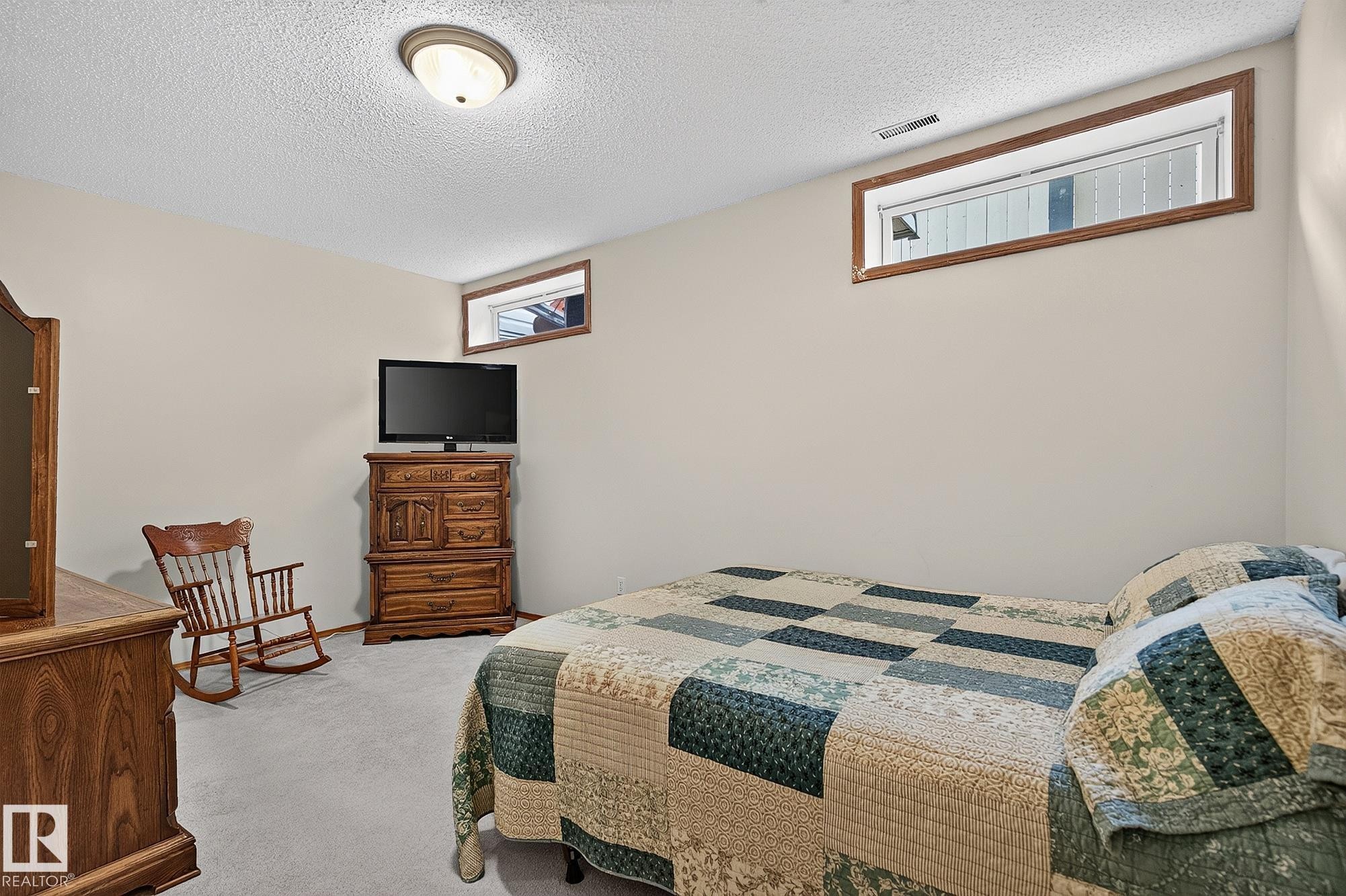 Bedroom 4 in the basement is a large carpeted room featuring a ceiling-mounted light fixture, two transom windows with wood trim, and neutral wall tones - 385 Meadowview Terrace, Sherwood Park, AB - Indoor Photo Showing Bedroom