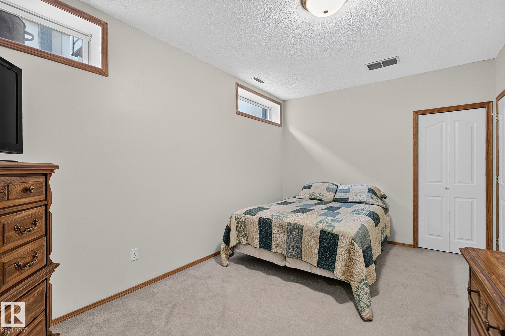 Bedroom 4 is a carpeted basement room featuring light-toned walls, a textured ceiling, and two upper-level windows with wood trim - 385 Meadowview Terrace, Sherwood Park, AB - Indoor Photo Showing Bedroom