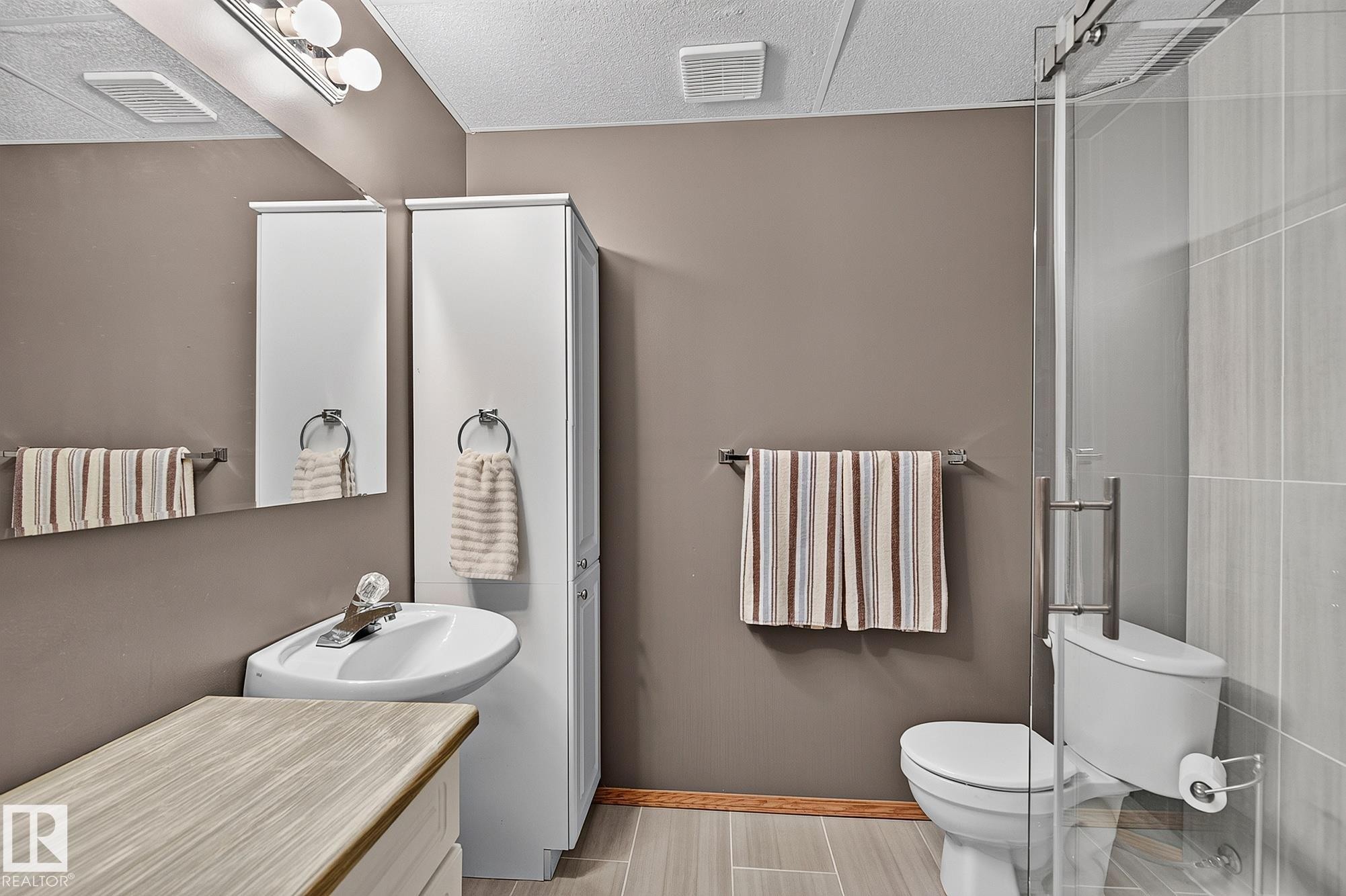 Contemporary 3-pc bathroom in the basement featuring a corner-mounted sink, a glass-enclosed shower, and a built-in storage cabinet - 385 Meadowview Terrace, Sherwood Park, AB - Indoor Photo Showing Bathroom