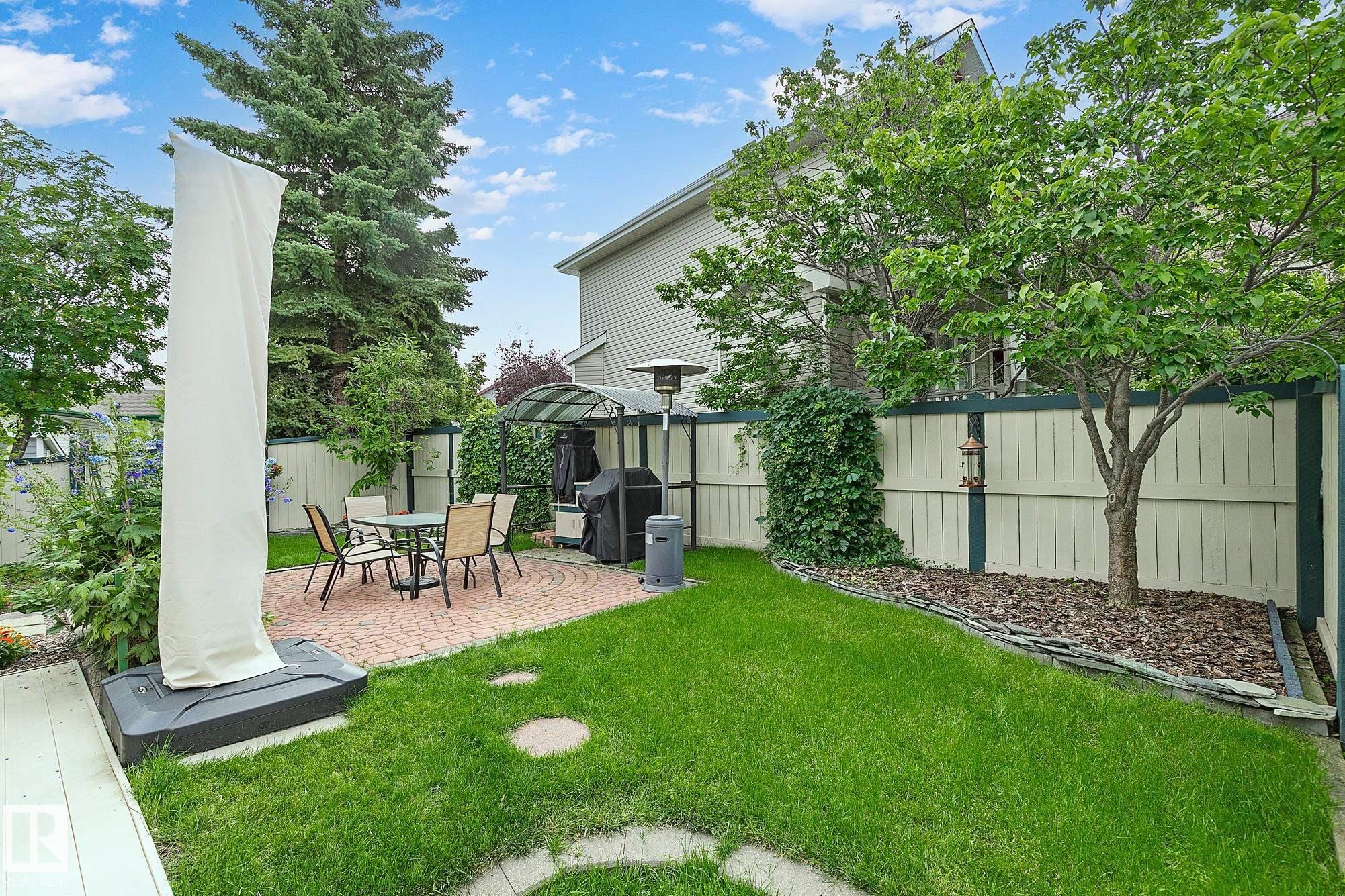 Manicured backyard featuring a circular brick patio, a gazebo, a green lawn, mature trees, and a privacy fence - 385 Meadowview Terrace, Sherwood Park, AB - Outdoor