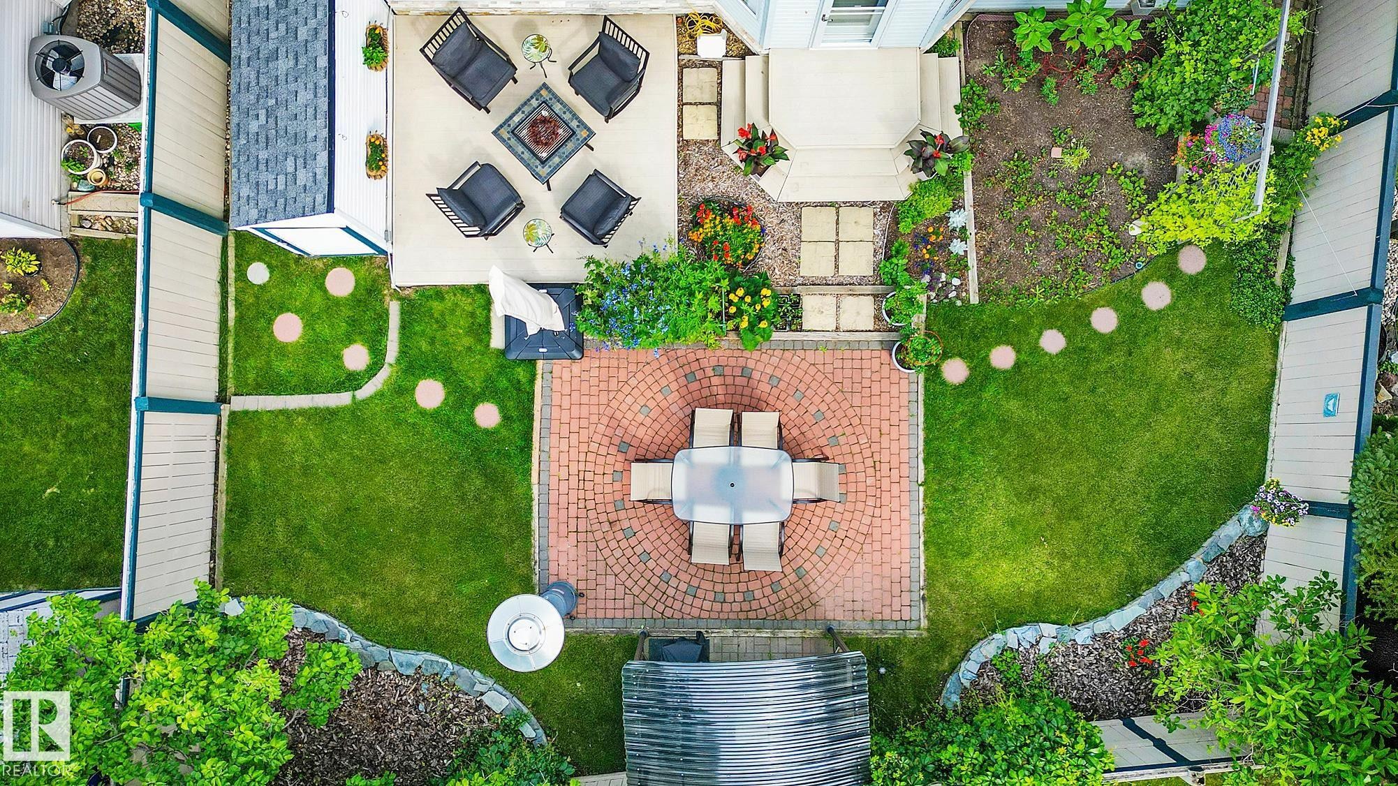 Aerial view of a sophisticated outdoor living space featuring a brick-paved central patio with dining table, surrounded by manicured lawn with decorative white pavers creating defined pathways - 385 Meadowview Terrace, Sherwood Park, AB -