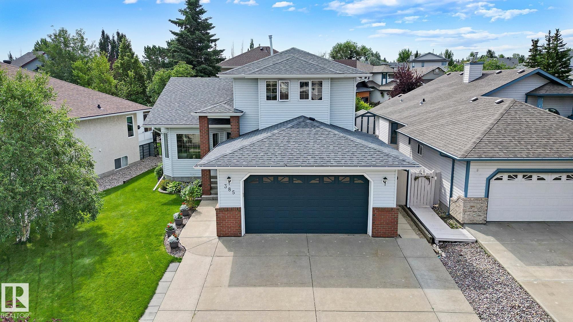 Light-coloured siding exterior featuring a dark garage door, brick accents, a shingled roof, and a large concrete driveway - 385 Meadowview Terrace, Sherwood Park, AB - Outdoor With Facade