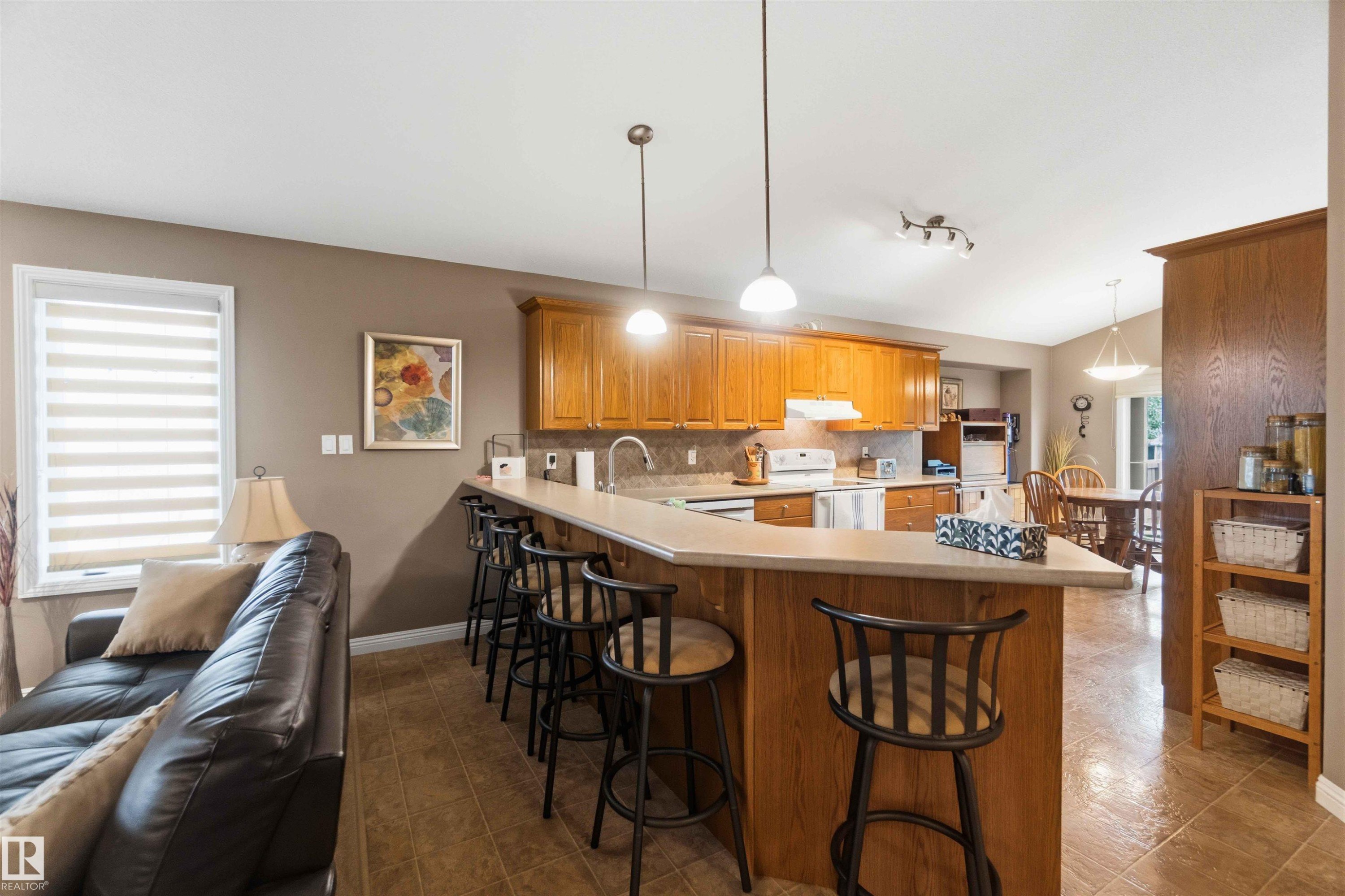 Kitchen featuring wood-finish cabinetry, stainless steel appliances, and a breakfast bar with pendant lighting - 6320 166 Avenue Nw, Edmonton, AB - Indoor