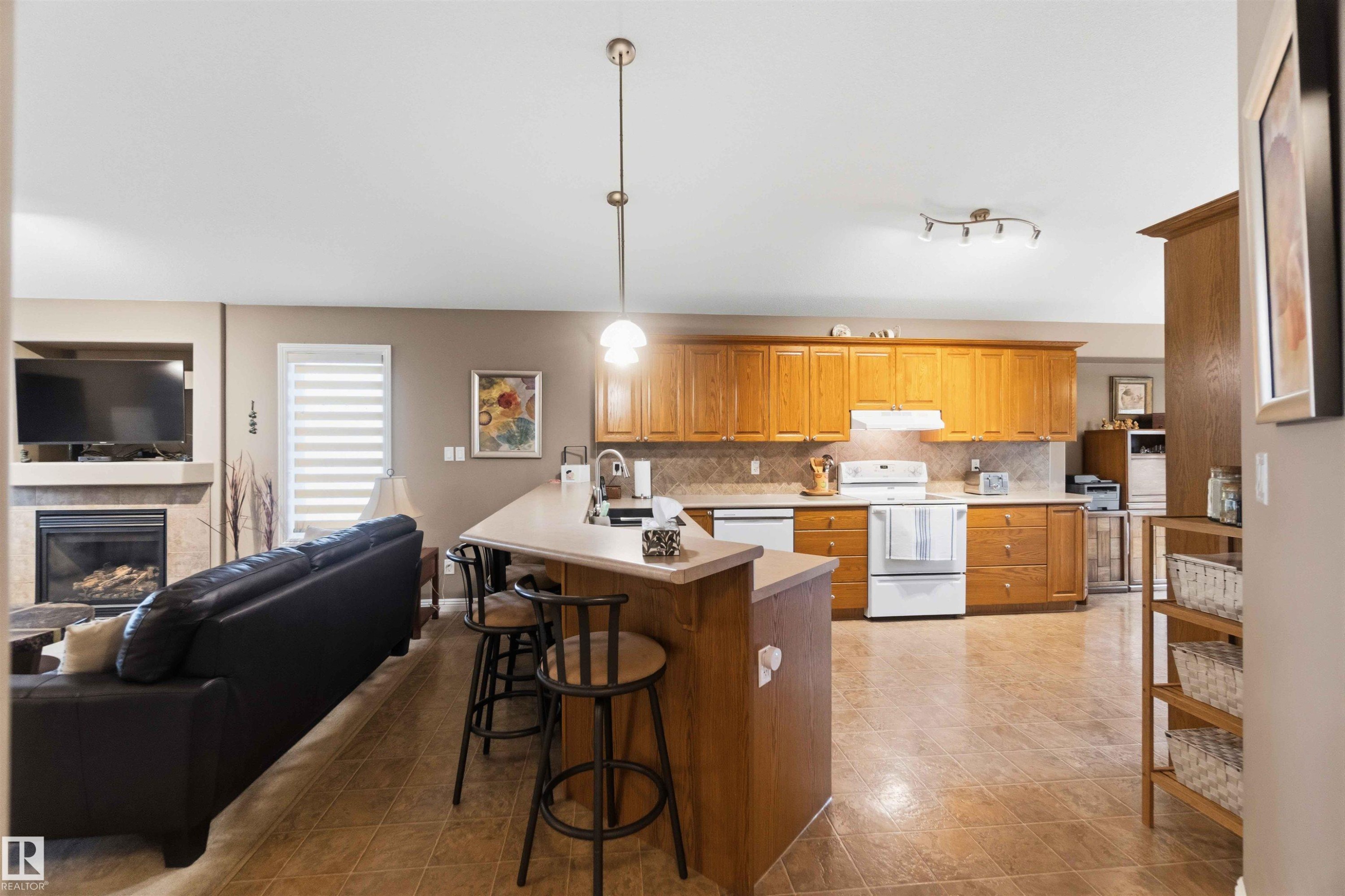 Open-concept kitchen featuring light-toned wood cabinetry, white appliances, and a tiled backsplash - 6320 166 Avenue Nw, Edmonton, AB - Indoor Photo Showing Kitchen With Fireplace