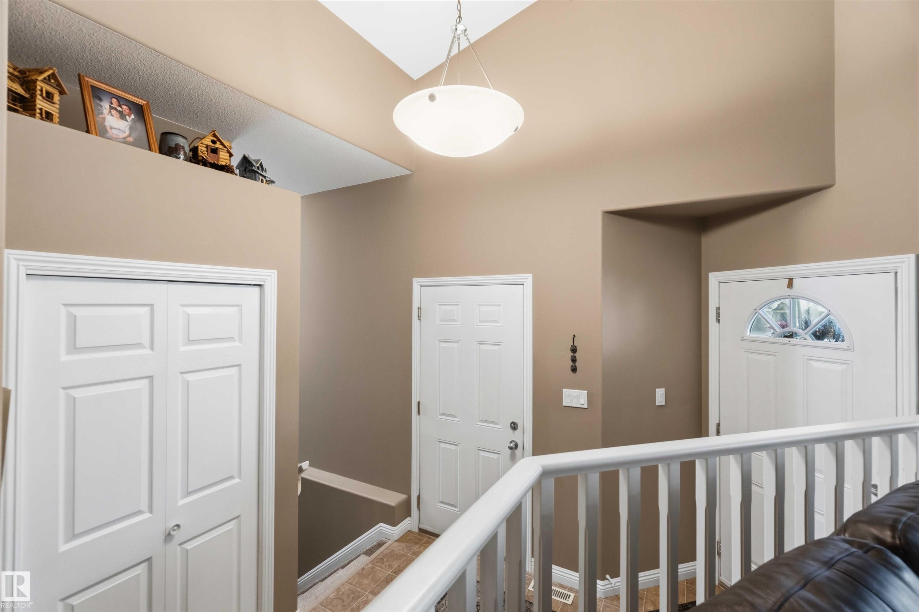 Foyer featuring a vaulted ceiling with a semi-flush mount fixture, a decorative ledge, white paneled doors, and a staircase with a white railing - 6320 166 Avenue Nw, Edmonton, AB - Indoor Photo Showing Other Room