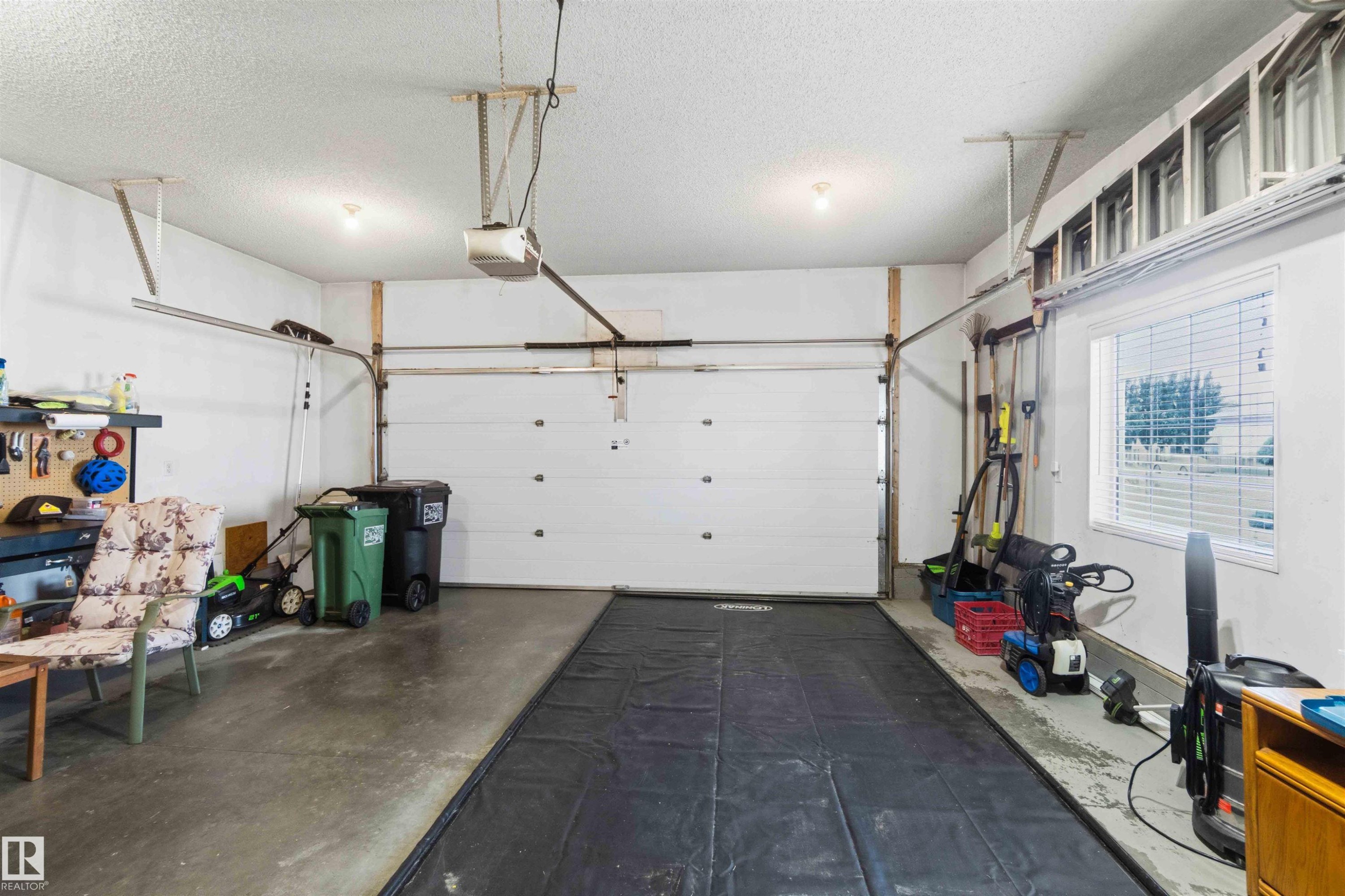Spacious garage featuring a concrete floor, overhead lighting, and a window with blinds - 6320 166 Avenue Nw, Edmonton, AB - Indoor Photo Showing Garage