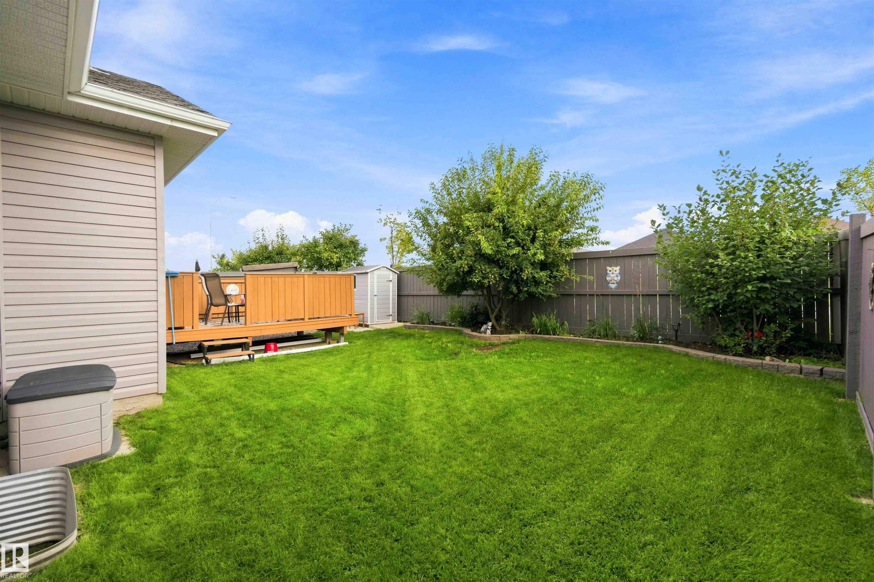 Expansive green lawn with a wood deck, perimeter fencing, and mature landscaping - 6320 166 Avenue Nw, Edmonton, AB - Outdoor With Deck Patio Veranda