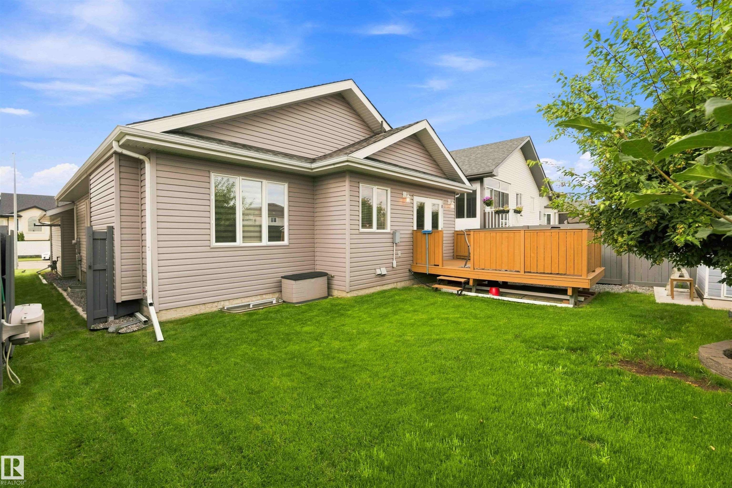 Spacious green lawn with a wooden deck featuring a privacy fence, light tan siding, and white-trimmed windows - 6320 166 Avenue Nw, Edmonton, AB - Outdoor With Deck Patio Veranda