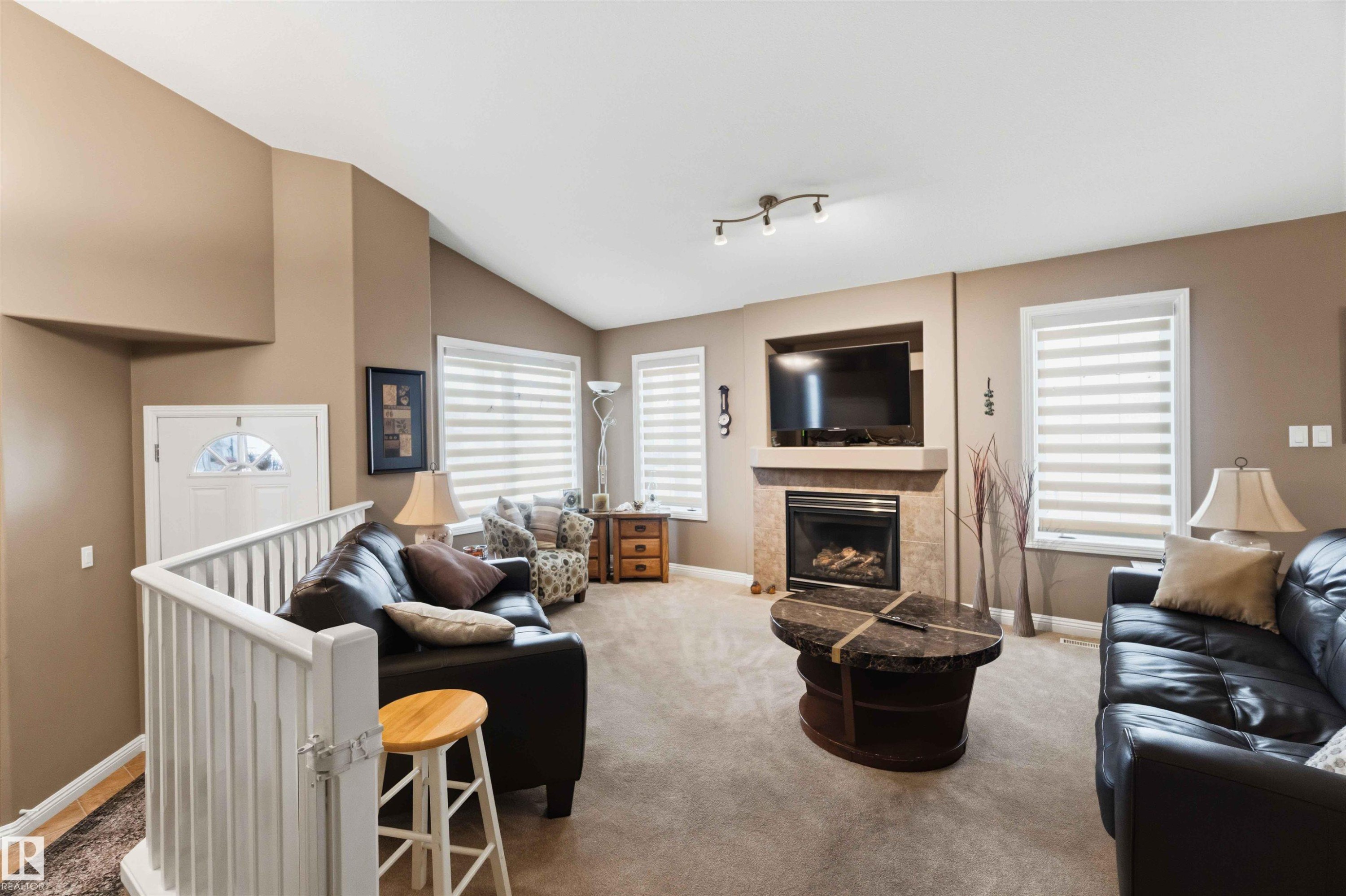 Spacious living area featuring a vaulted ceiling and neutral-toned carpet - 6320 166 Avenue Nw, Edmonton, AB - Indoor Photo Showing Living Room With Fireplace