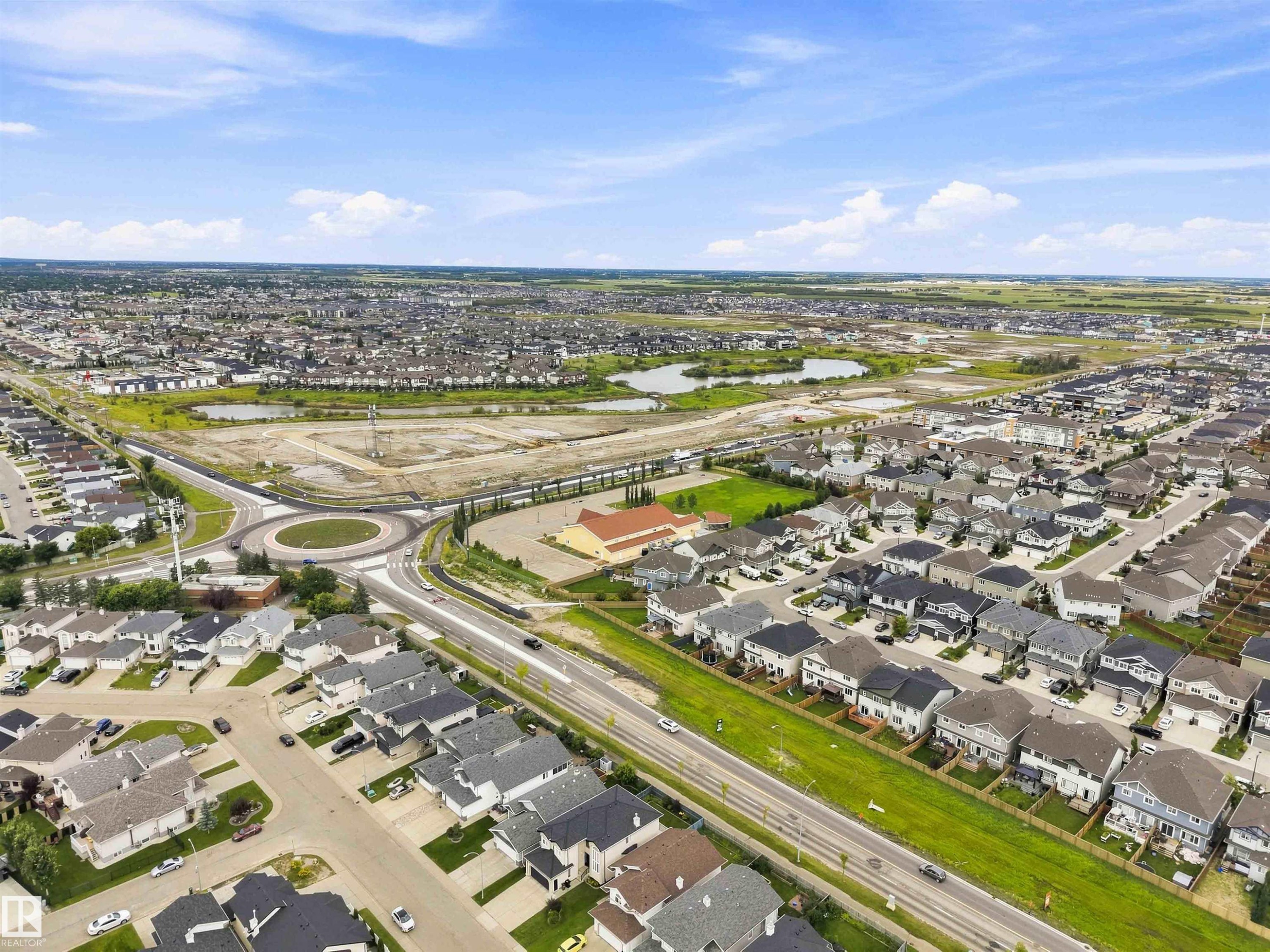 Aerial perspective showcasing a residential development with multiple single-family homes, a prominent roundabout, and roadways - 6320 166 Avenue Nw, Edmonton, AB - Outdoor With View