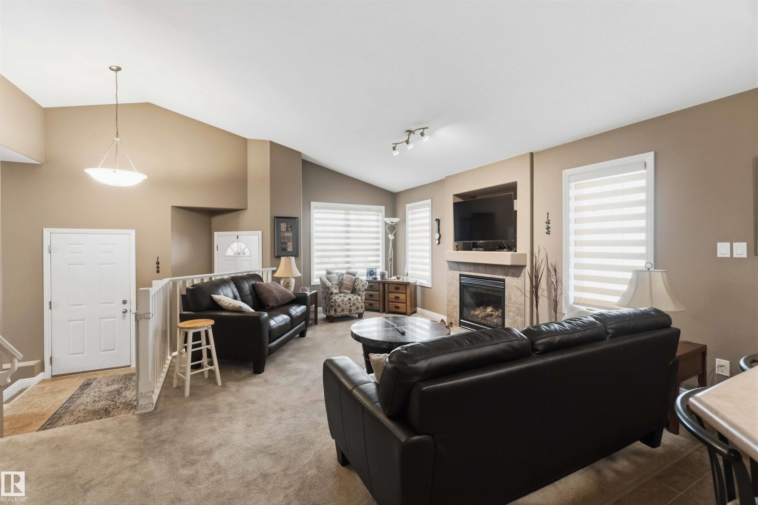 Living room with vaulted ceiling, recessed fireplace with mantel, carpeted flooring, and multiple windows with horizontal blinds - 6320 166 Avenue Nw, Edmonton, AB - Indoor Photo Showing Living Room With Fireplace