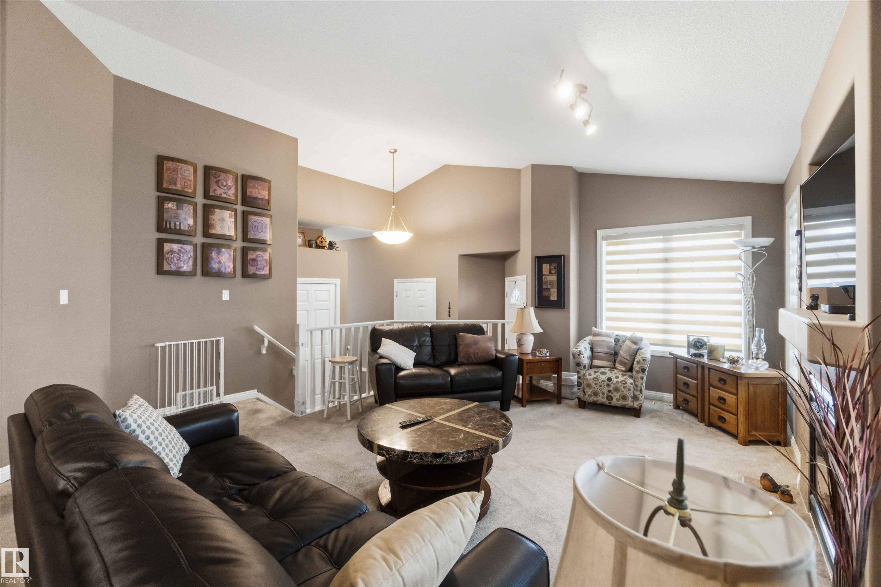 Spacious living area featuring vaulted ceilings, track lighting, and a stone-clad fireplace - 6320 166 Avenue Nw, Edmonton, AB - Indoor Photo Showing Living Room