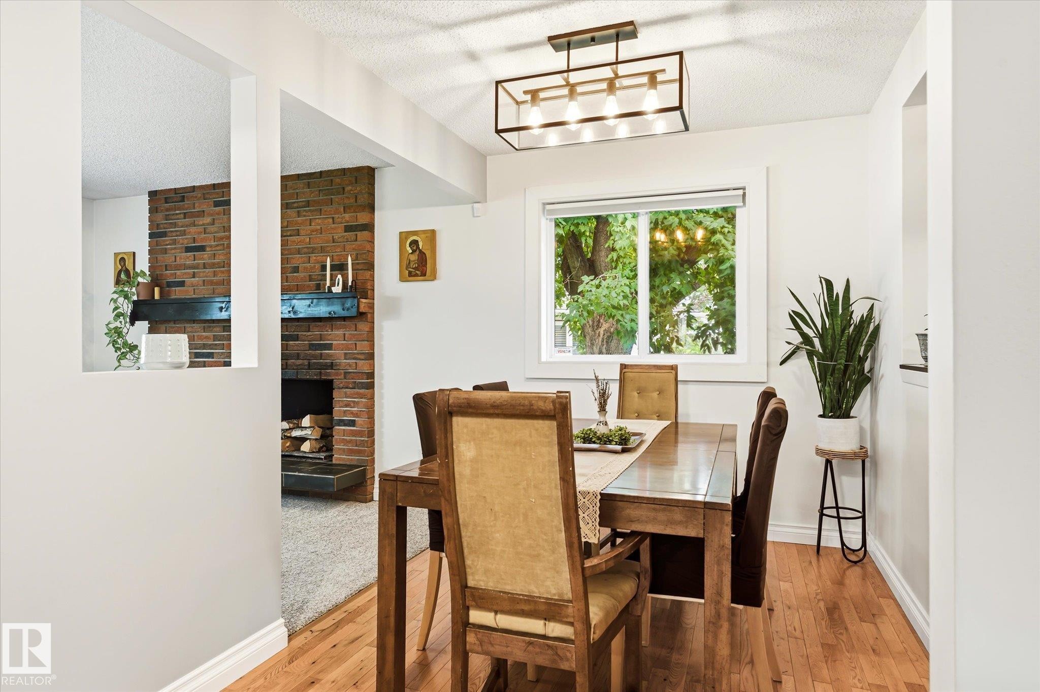 Dining area featuring wood-finish flooring, a white window frame, and a contemporary linear chandelier - 4921 47 Avenue, Legal, AB - Indoor Photo Showing Dining Room