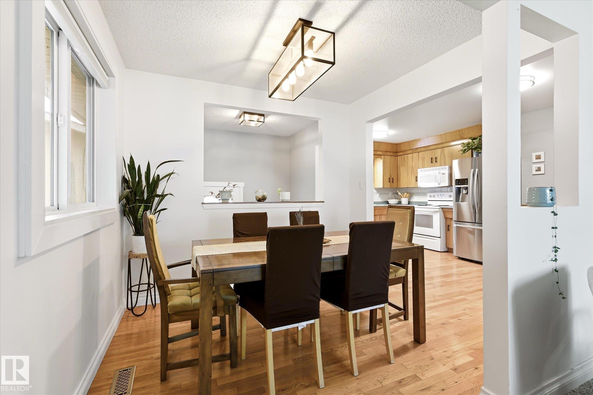 Dining area featuring wood-finish flooring, a contemporary linear chandelier, and a bright window - 4921 47 Avenue, Legal, AB - Indoor Photo Showing Dining Room