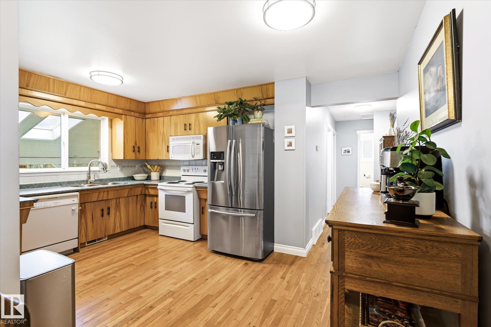 Kitchen featuring wood-finish cabinetry, stainless steel refrigerator, white electric range, and dishwasher - 4921 47 Avenue, Legal, AB - Indoor Photo Showing Kitchen With Double Sink
