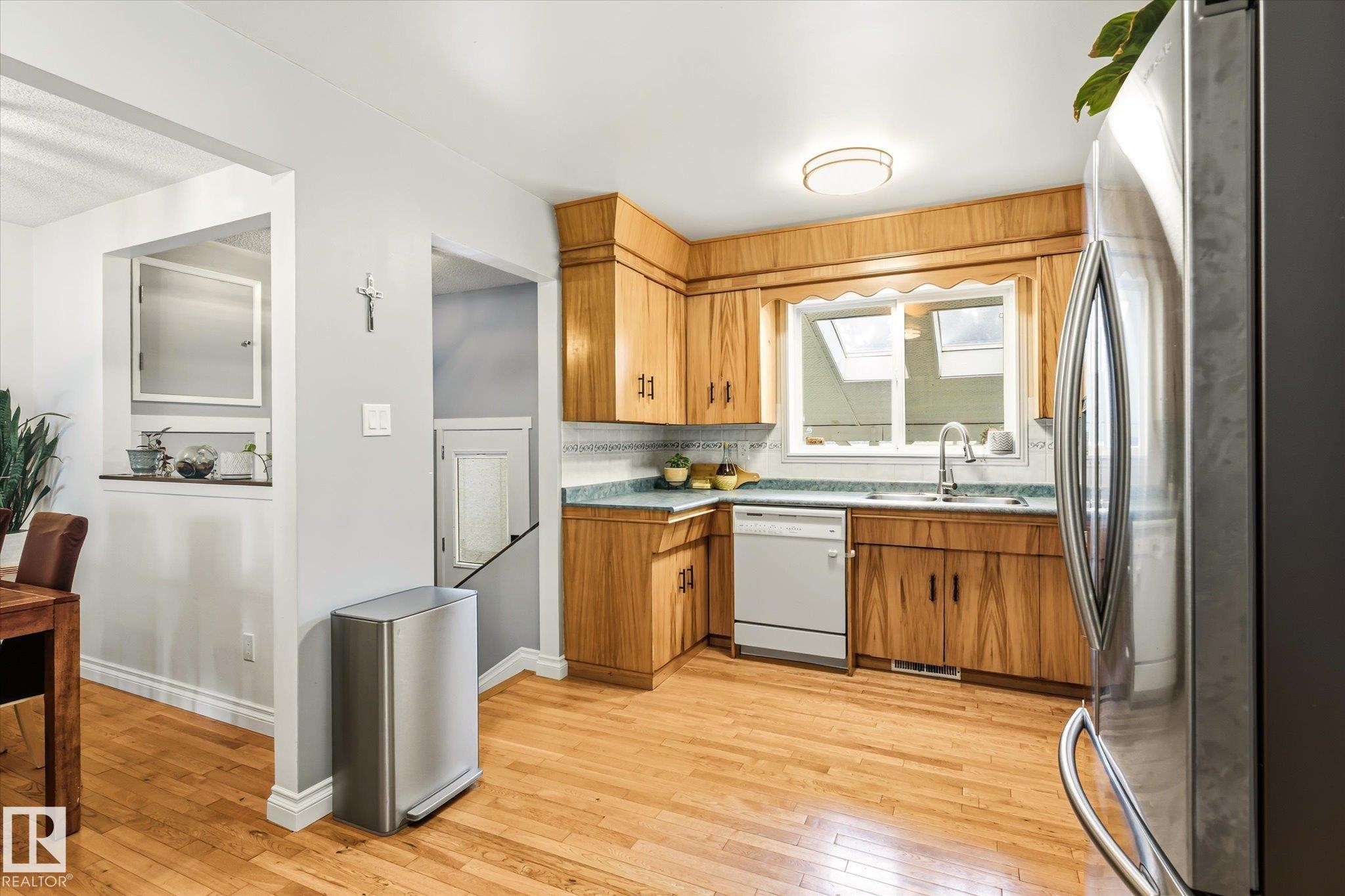 Kitchen featuring light wood cabinetry, a stainless steel refrigerator, and wood-finish flooring - 4921 47 Avenue, Legal, AB - Indoor Photo Showing Kitchen With Double Sink