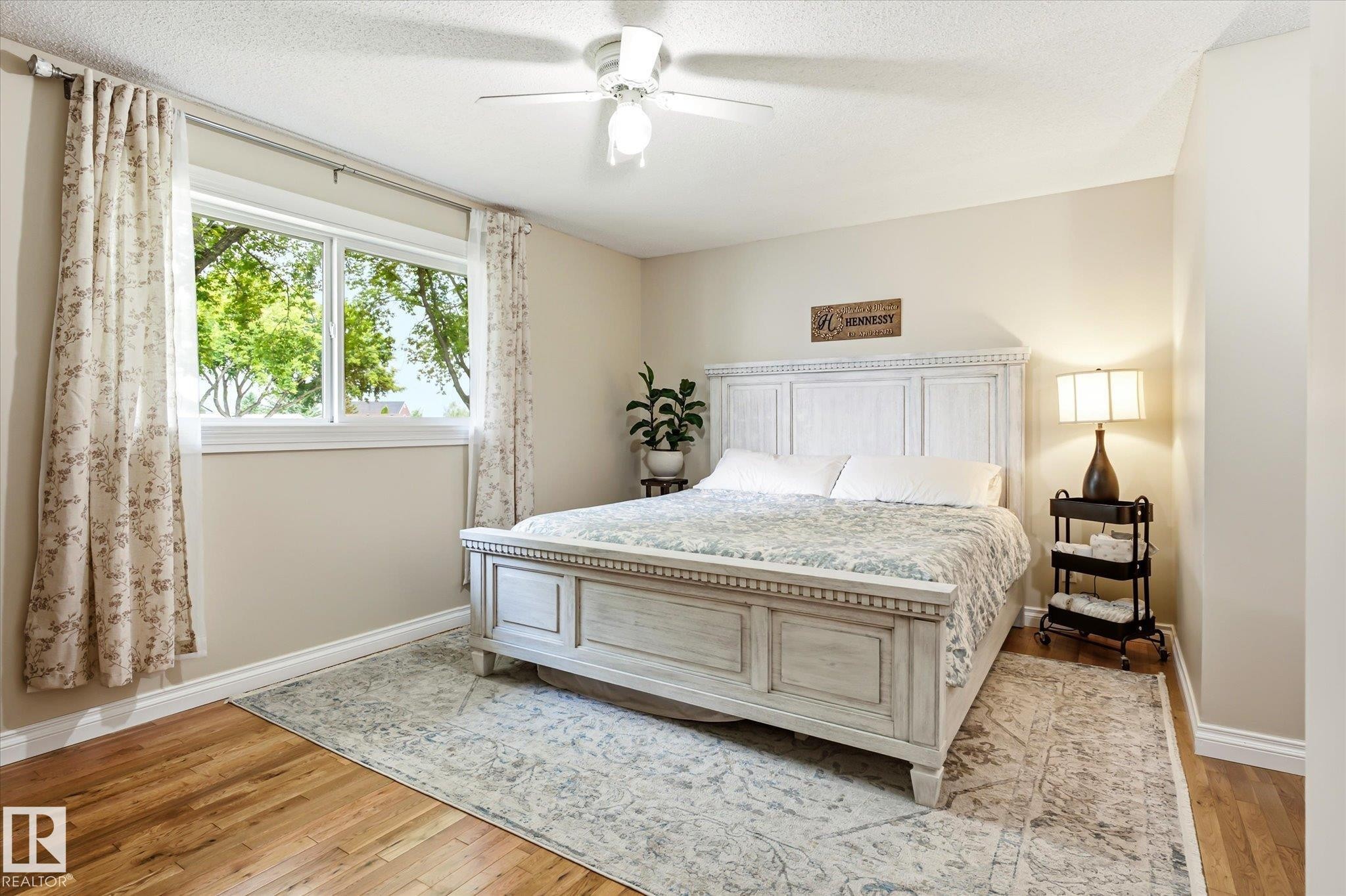 Spacious room featuring wood-finish flooring, a large window, a ceiling fan with integrated lighting, neutral wall tones, and white trim - 4921 47 Avenue, Legal, AB - Indoor Photo Showing Bedroom