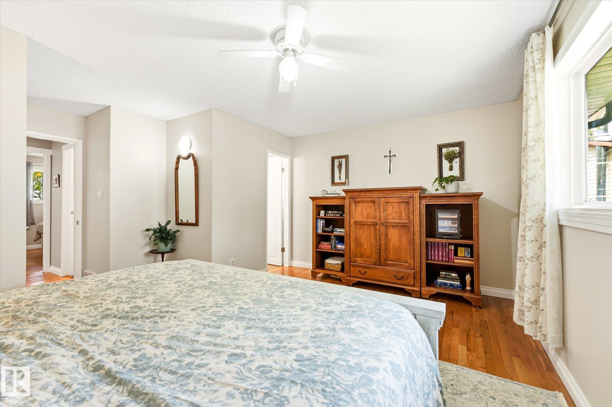 Bright room featuring wood-finish flooring, a ceiling fan with integrated lighting, and multiple windows with white trim - 4921 47 Avenue, Legal, AB - Indoor Photo Showing Bedroom