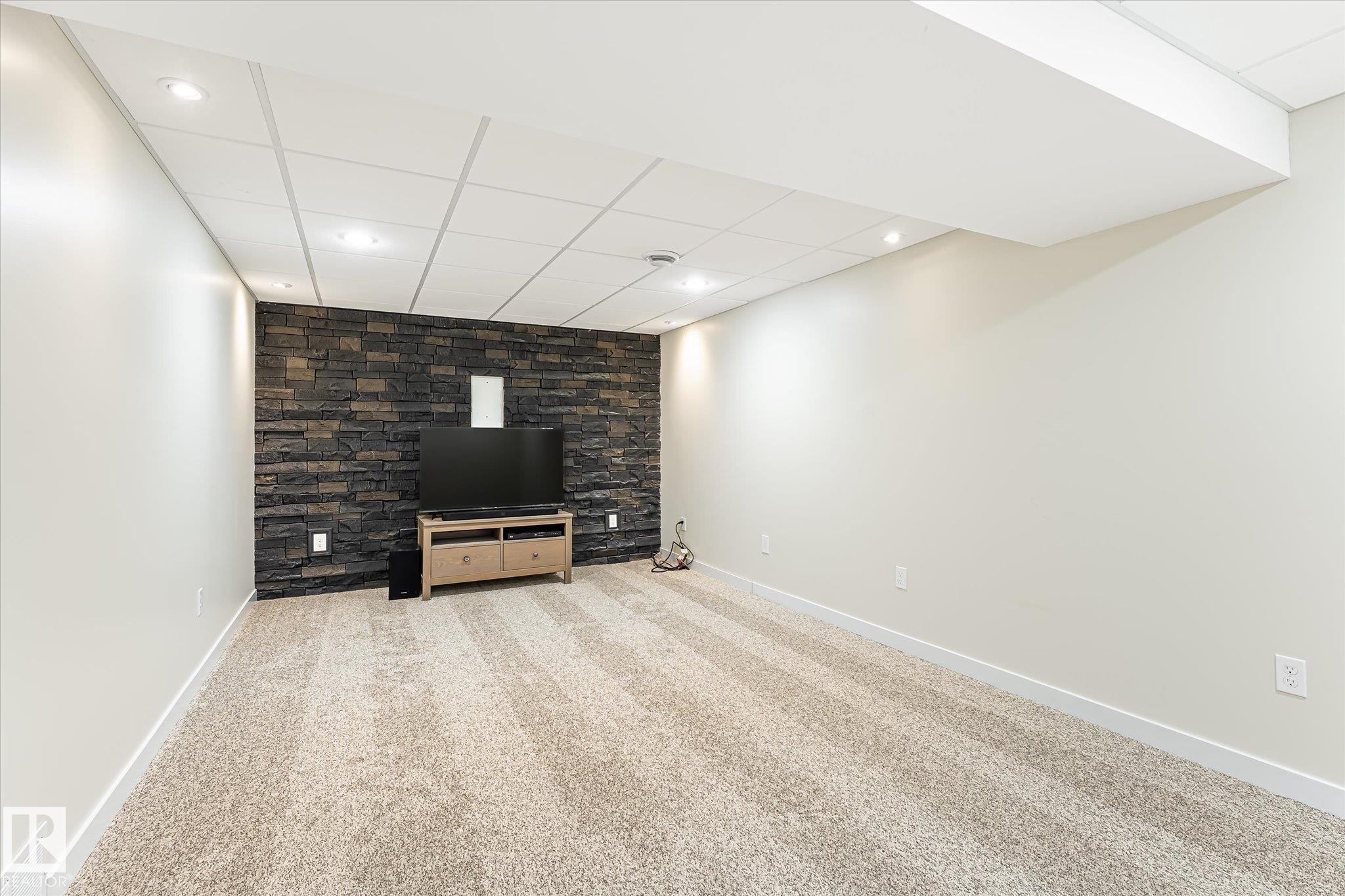 Finished room featuring a stone accent wall, recessed lighting, and neutral-toned carpeting - 4921 47 Avenue, Legal, AB - Indoor
