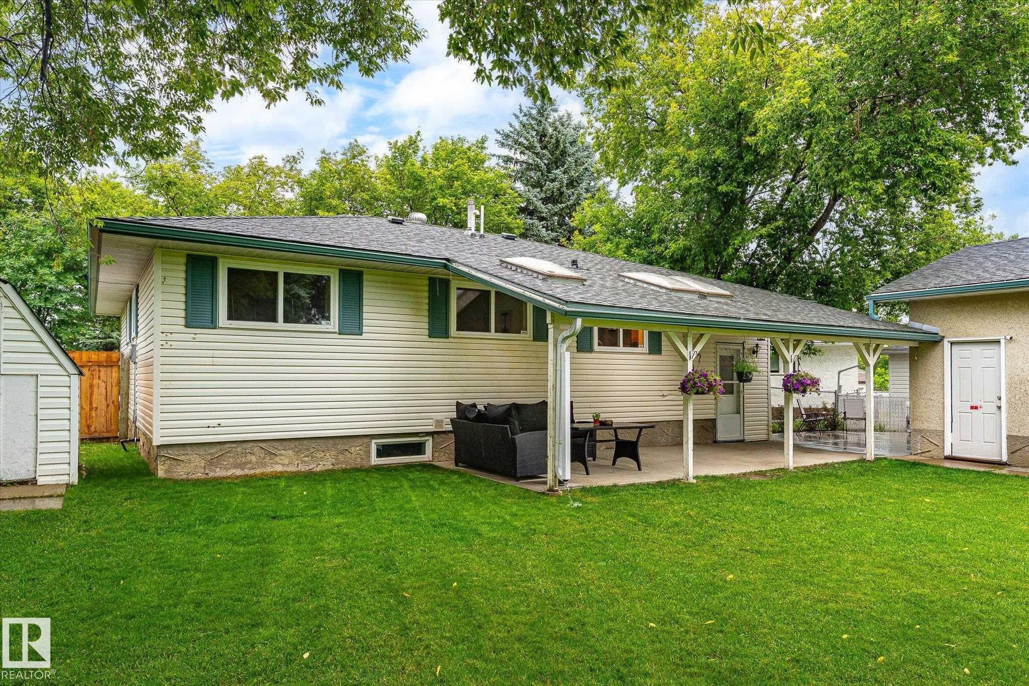 Expansive green lawn featuring a covered patio, skylights, white horizontal siding, and a separate storage shed - 4921 47 Avenue, Legal, AB - Outdoor