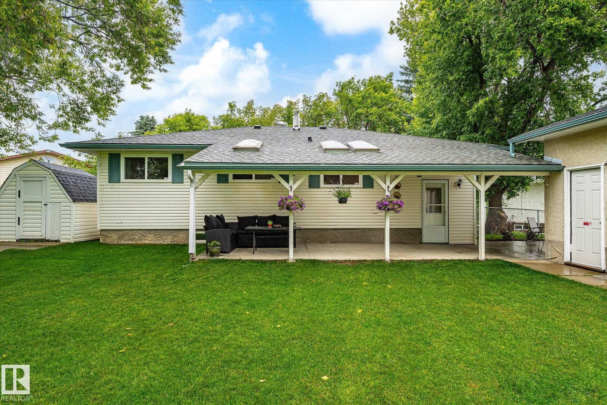 Spacious backyard featuring a covered patio, multiple skylights, a separate utility shed, and mature perimeter trees - 4921 47 Avenue, Legal, AB - Outdoor