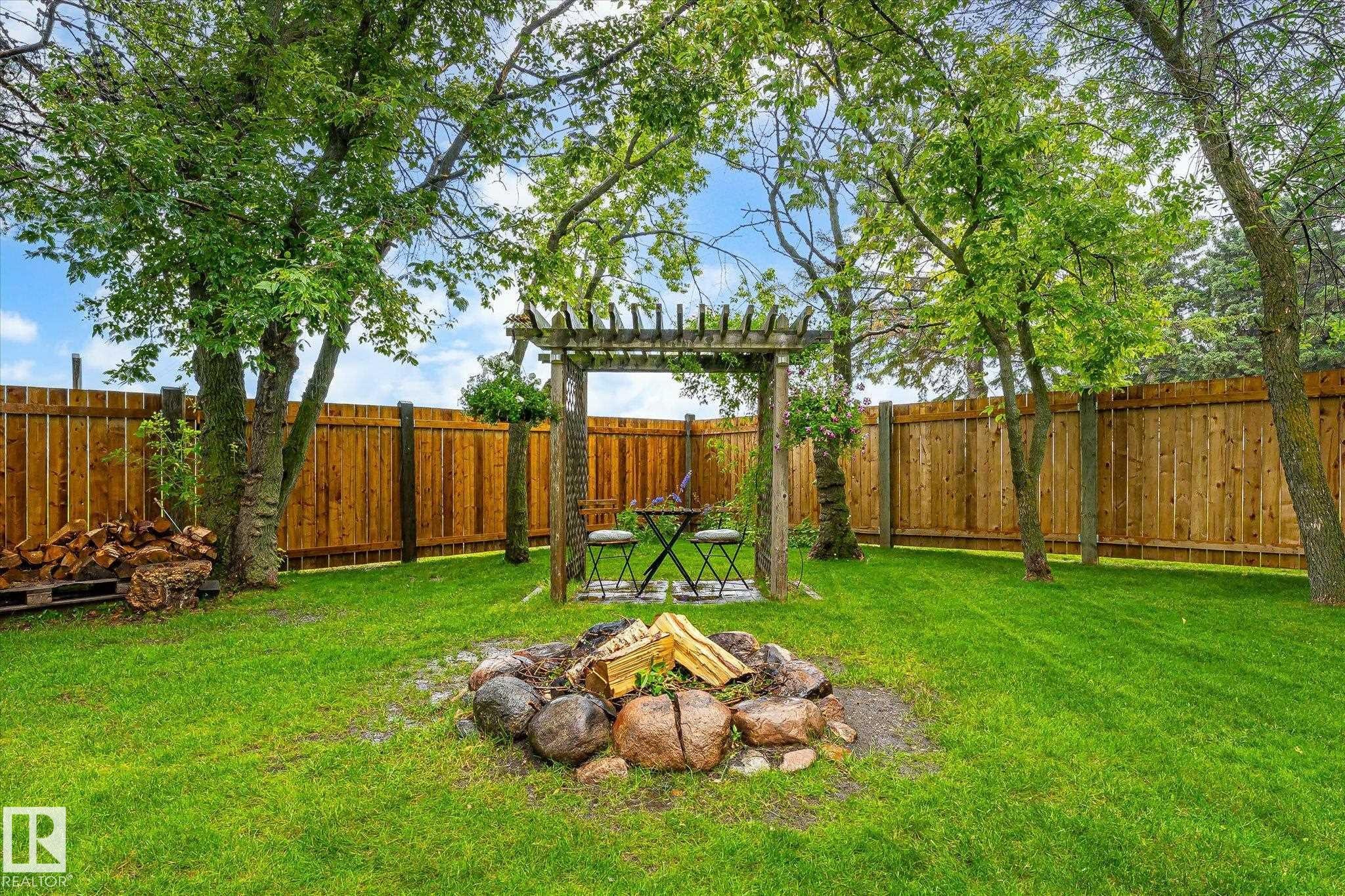 Expansive green lawn with a rock fire pit and a wooden pergola structure - 4921 47 Avenue, Legal, AB - Outdoor With Backyard