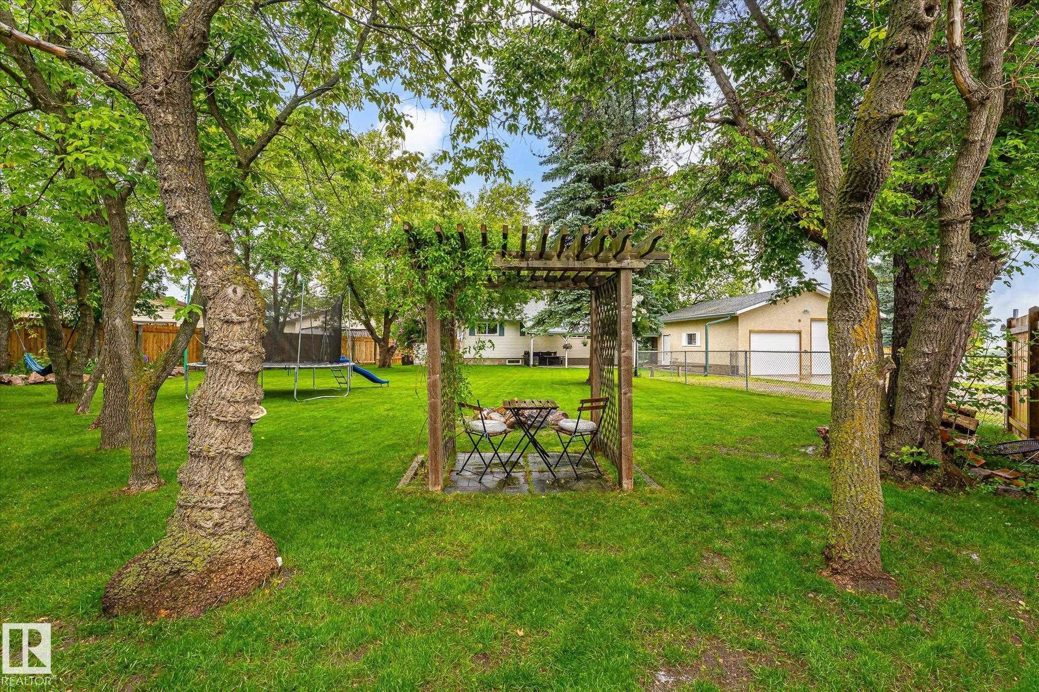 Expansive green lawn with mature trees and a wooden pergola structure - 4921 47 Avenue, Legal, AB - Outdoor With Backyard