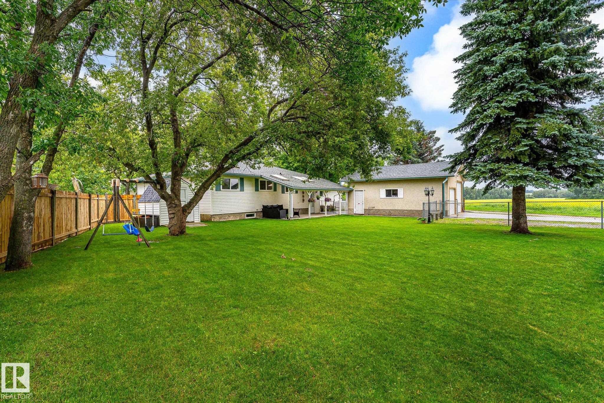 Expansive green lawn with mature trees and a wooden privacy fence - 4921 47 Avenue, Legal, AB - Outdoor
