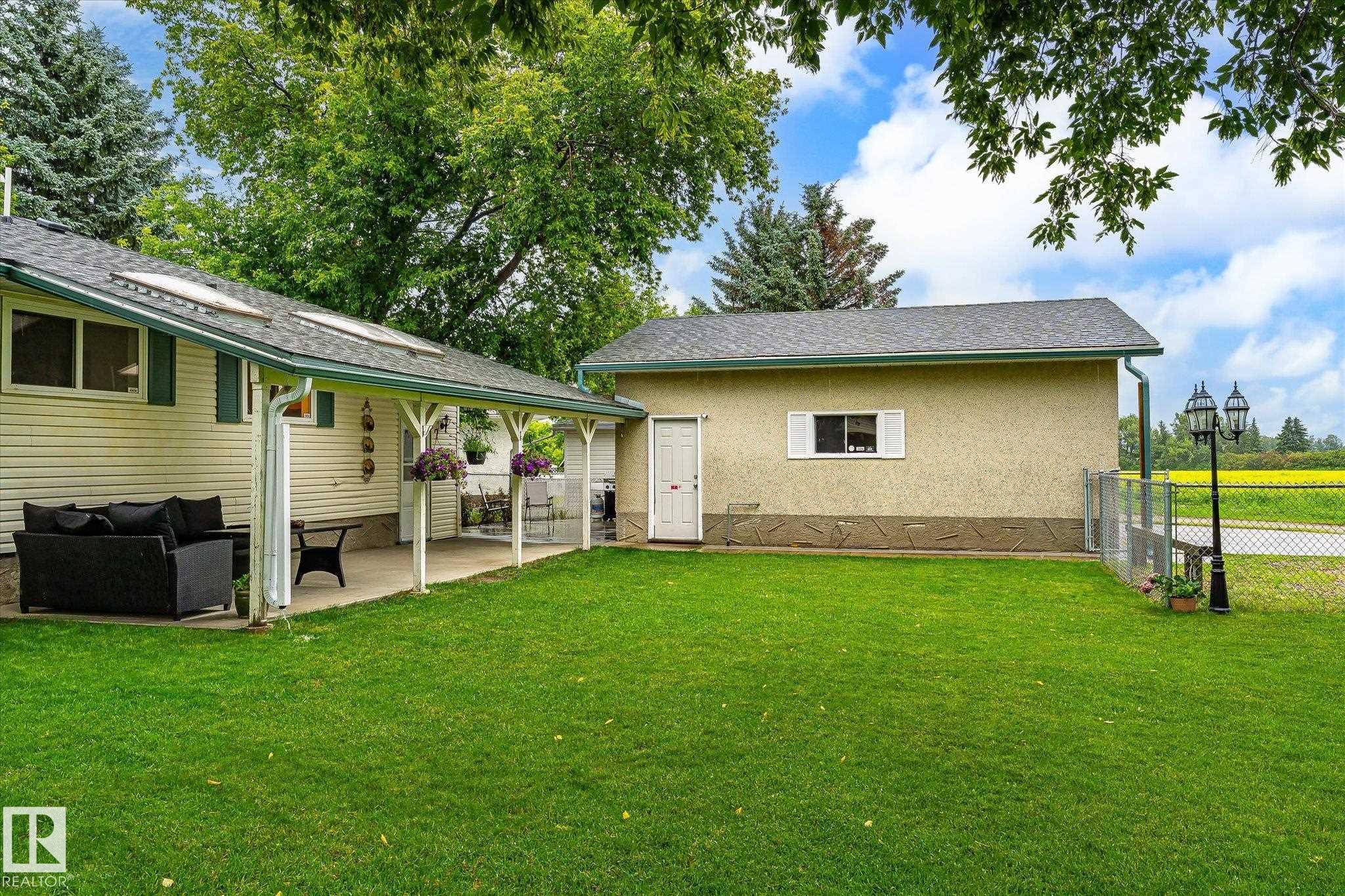 Expansive backyard featuring a lush lawn, covered patio, and a detached structure with stucco siding - 4921 47 Avenue, Legal, AB - Outdoor