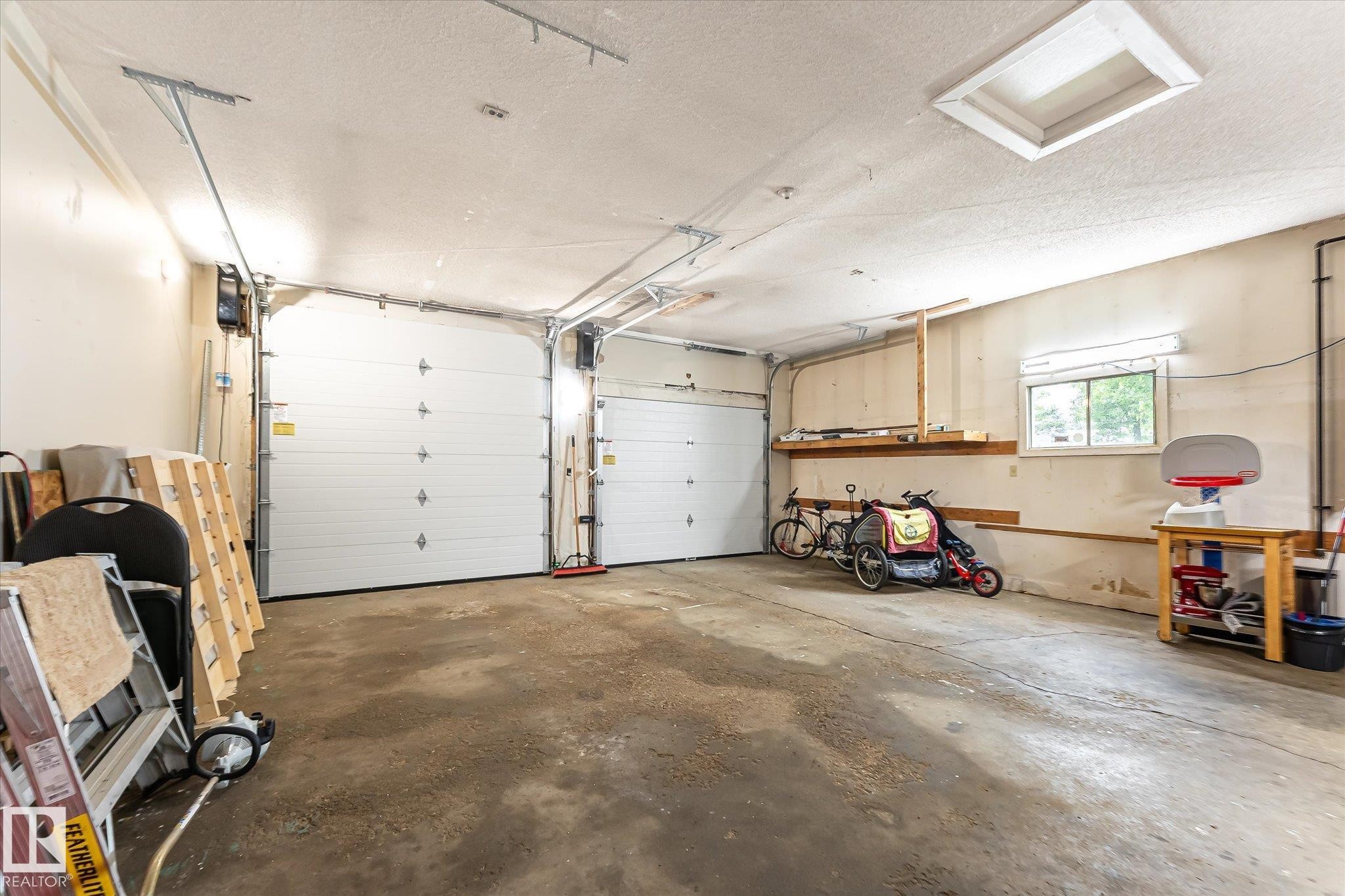 Attached two-car garage with concrete flooring, two automatic overhead doors, and built-in wall shelving - 4921 47 Avenue, Legal, AB - Indoor Photo Showing Garage
