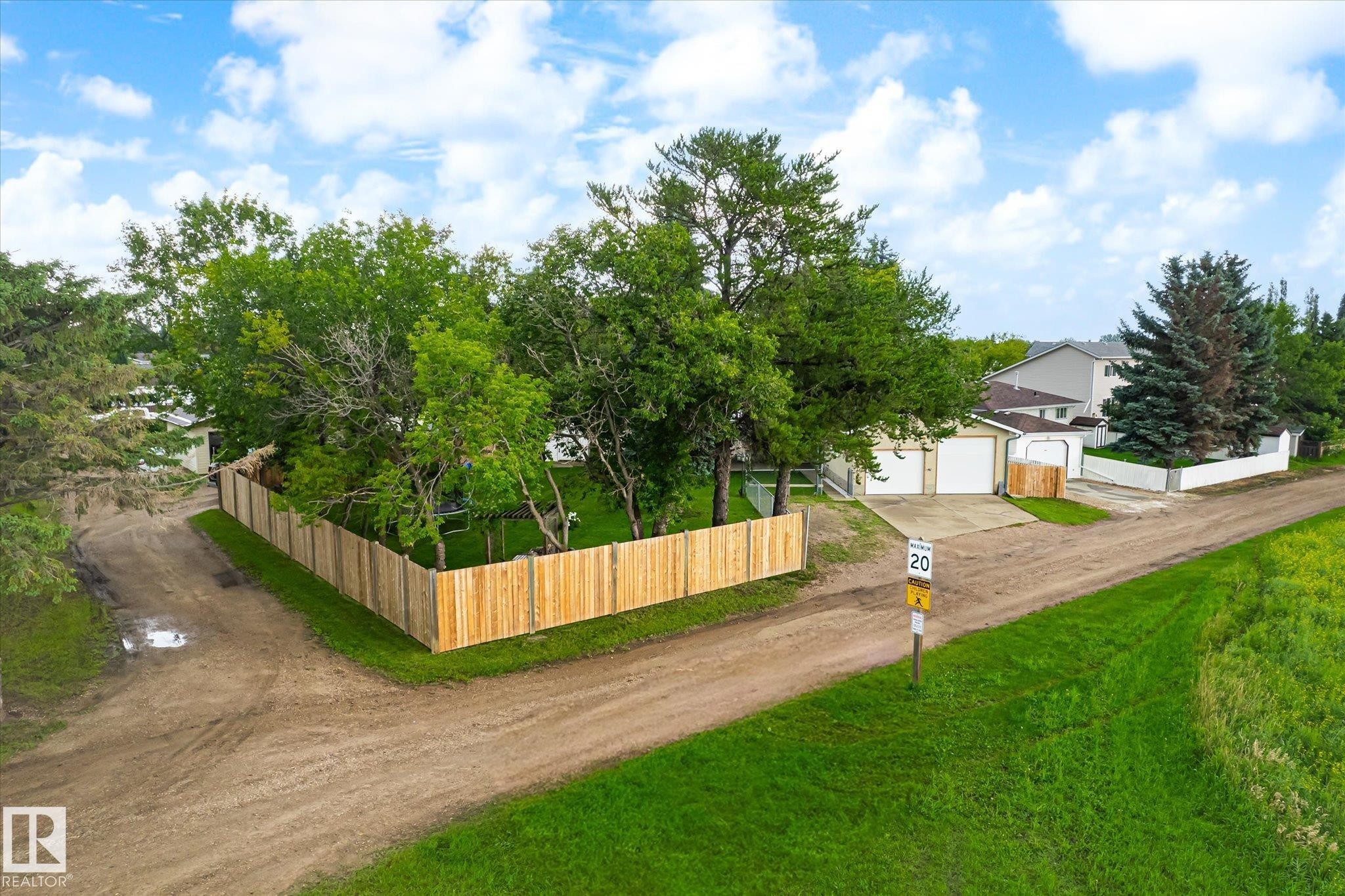 Property featuring a newly installed perimeter fence, mature trees, and a concrete driveway - 4921 47 Avenue, Legal, AB - Outdoor