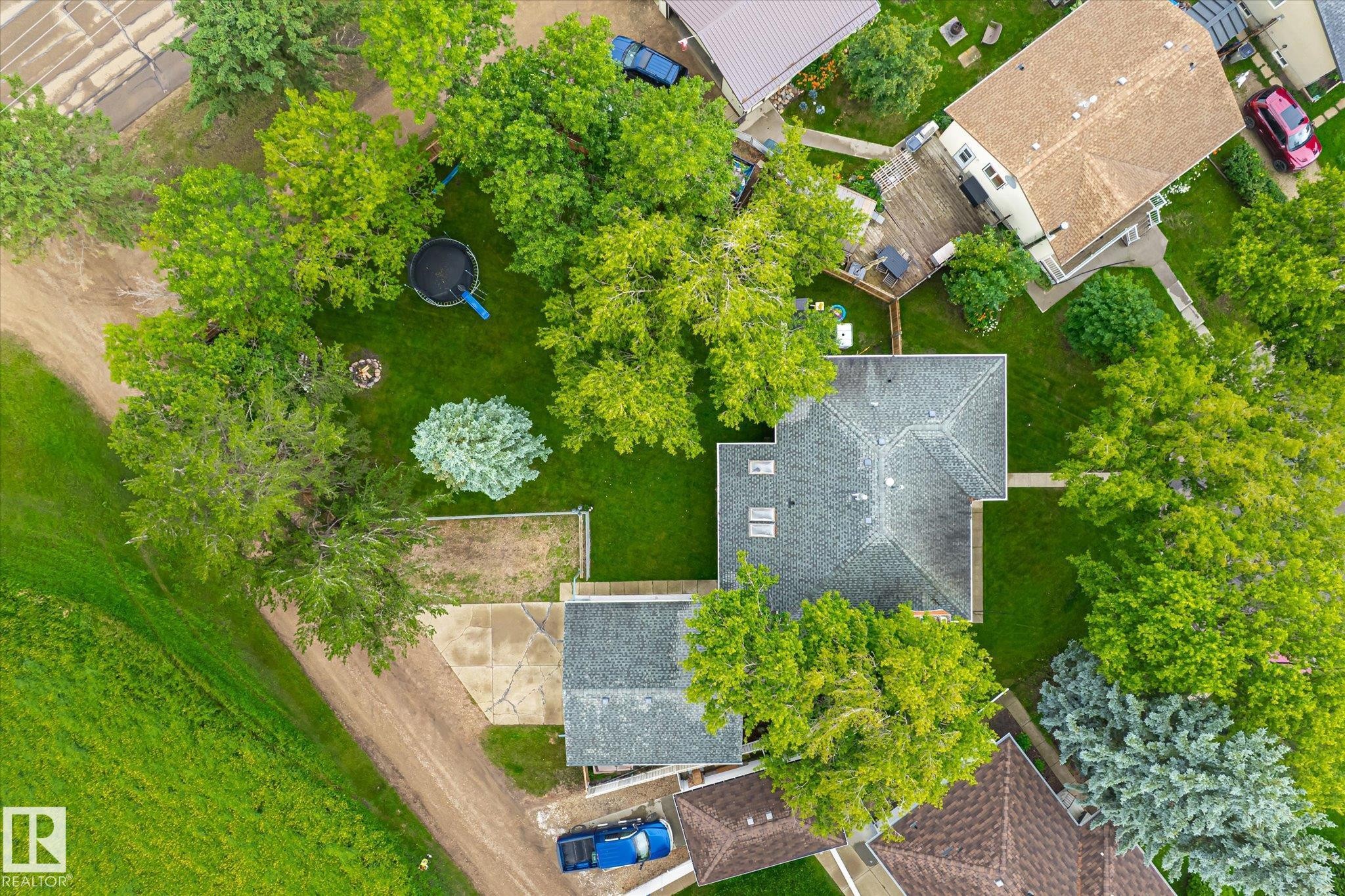 Aerial perspective showcasing a property surrounded by mature trees, featuring a large grassy yard and a paved driveway - 4921 47 Avenue, Legal, AB - Outdoor