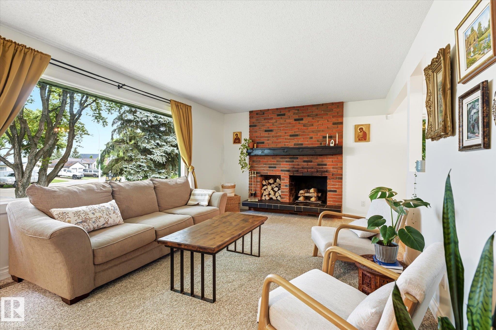 Living room featuring a brick fireplace with a wood mantle, a large picture window, and light-colored carpeting - 4921 47 Avenue, Legal, AB - Indoor Photo Showing Living Room With Fireplace