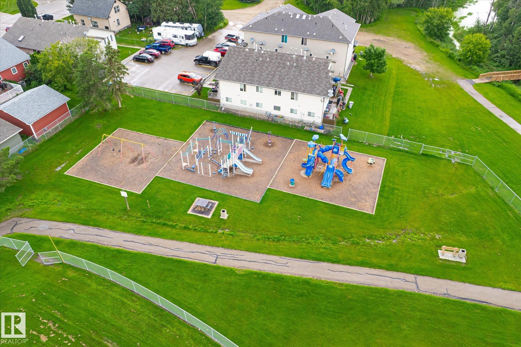 Community playground with multiple play structures and a swing set, bordered by a walking path and expansive green spaces - 4921 47 Avenue, Legal, AB - Outdoor