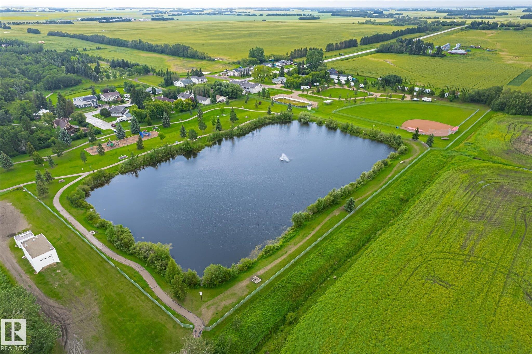 Aerial perspective showcasing a community park with a prominent pond and fountain feature - 4921 47 Avenue, Legal, AB - Outdoor With Body Of Water With View