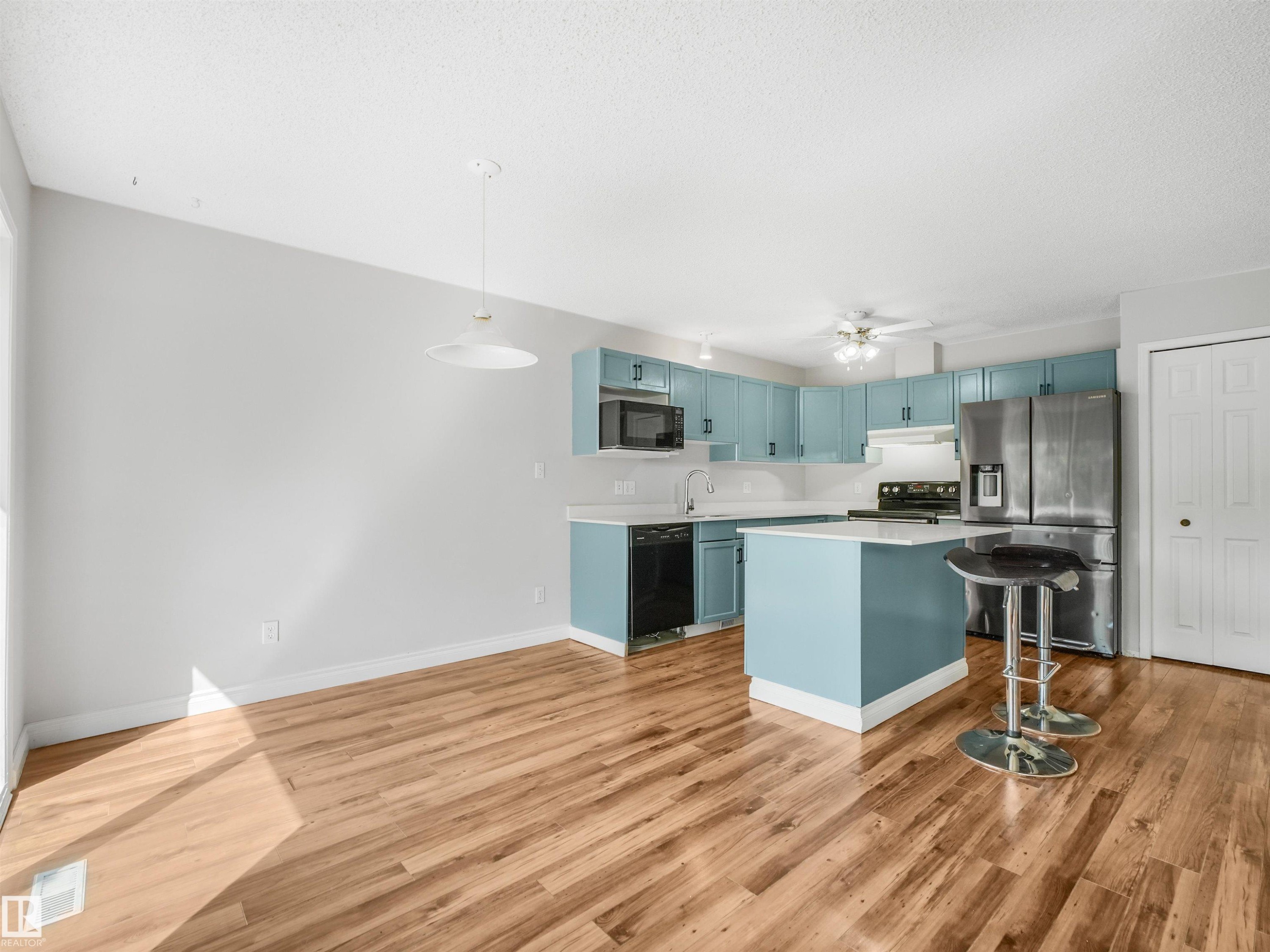Open-concept kitchen and dining area featuring wood-finish flooring, a kitchen island with seating, light blue cabinetry, and stainless steel appliances - #2 3311 58 St Nw, Edmonton, AB - Indoor Photo Showing Kitchen