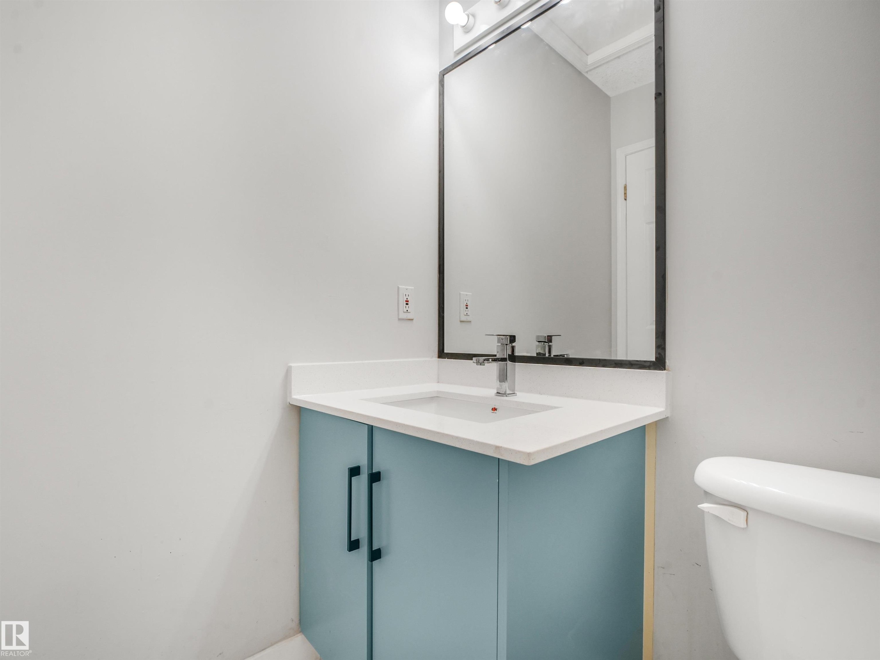 Vanity area featuring a light blue cabinet with black hardware, white countertop, and a rectangular sink with a chrome faucet - #2 3311 58 St Nw, Edmonton, AB - Indoor Photo Showing Bathroom