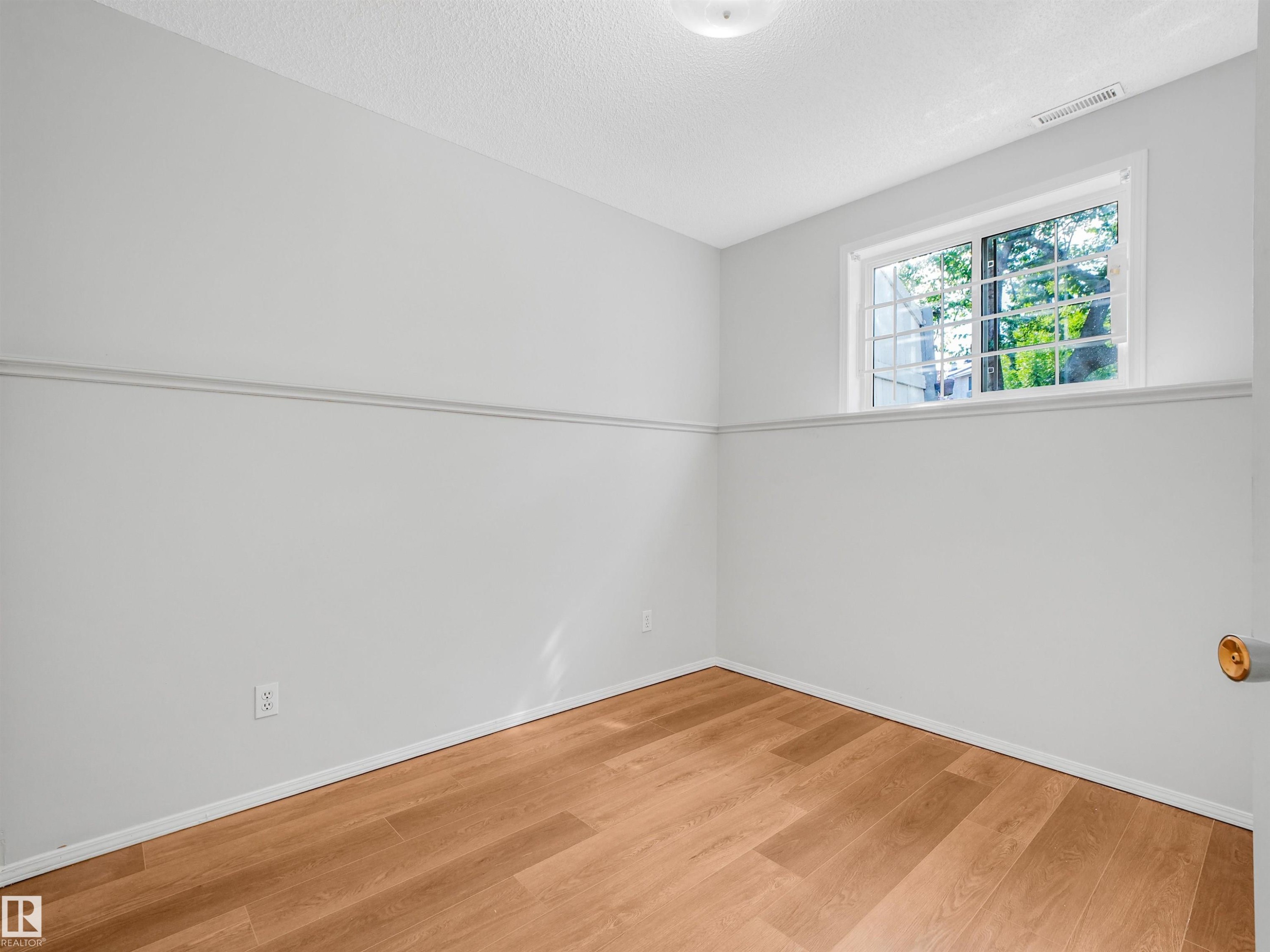 Room featuring light wood-finish flooring, light gray walls with a chair rail, a white-framed window with security bars, and a flush-mount ceiling light fixture - #2 3311 58 St Nw, Edmonton, AB - Indoor Photo Showing Other Room