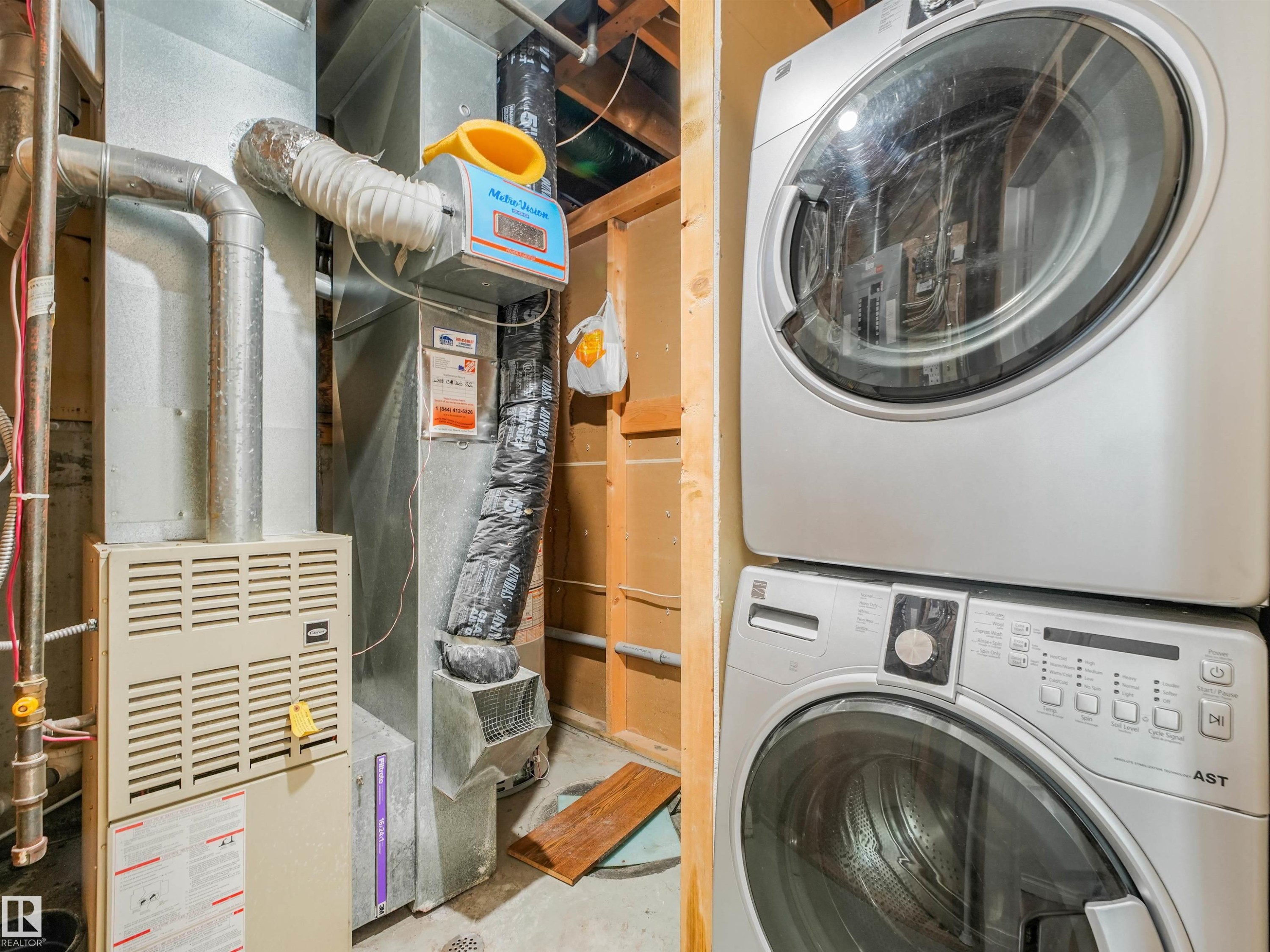 Utility area featuring a furnace system with galvanized ductwork, associated piping, and a stacked washer and dryer unit - #2 3311 58 St Nw, Edmonton, AB - Indoor Photo Showing Laundry Room