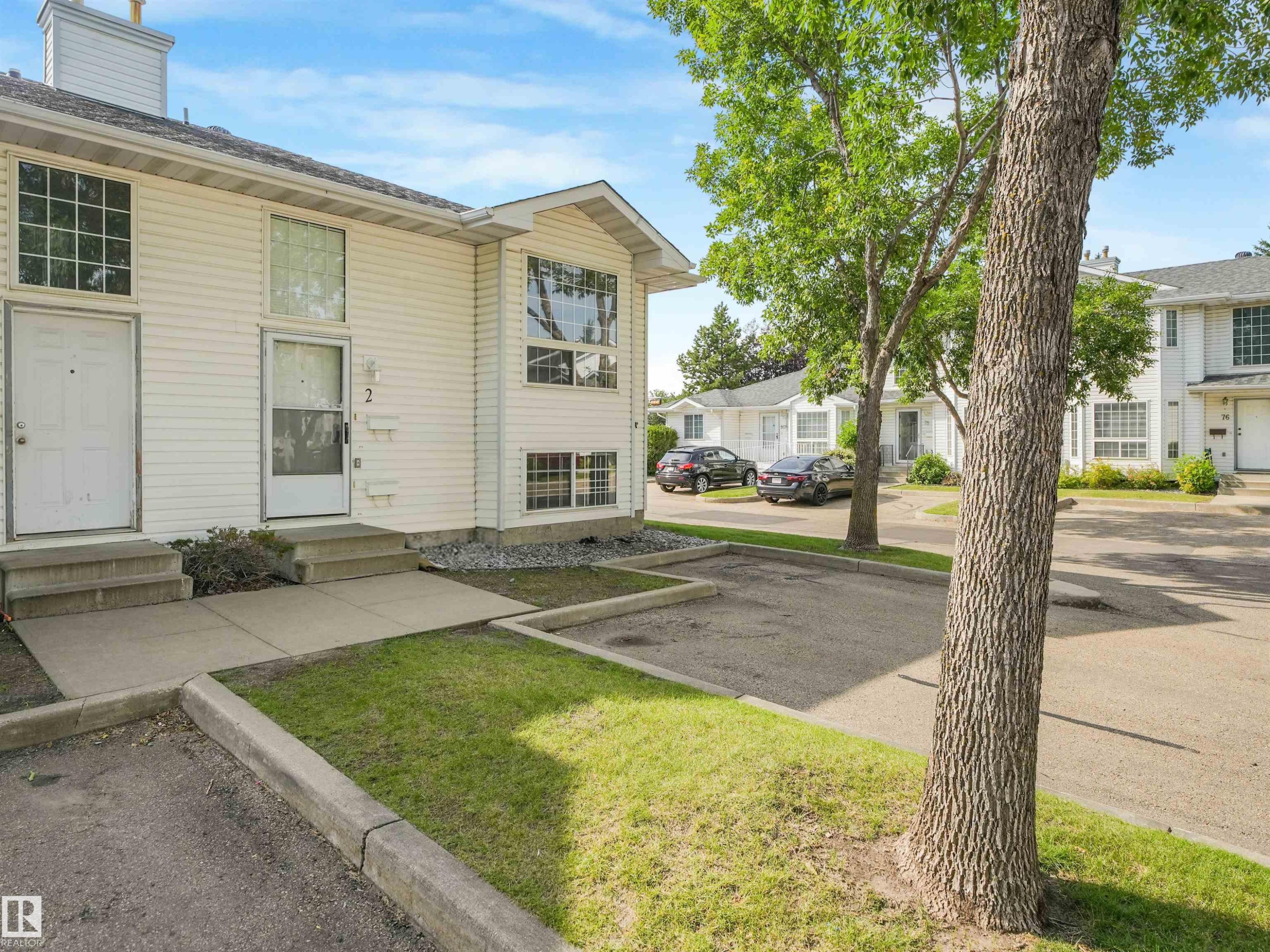 White siding exterior with multiple windows, featuring an entryway with a white door and concrete steps - #2 3311 58 St Nw, Edmonton, AB - Outdoor