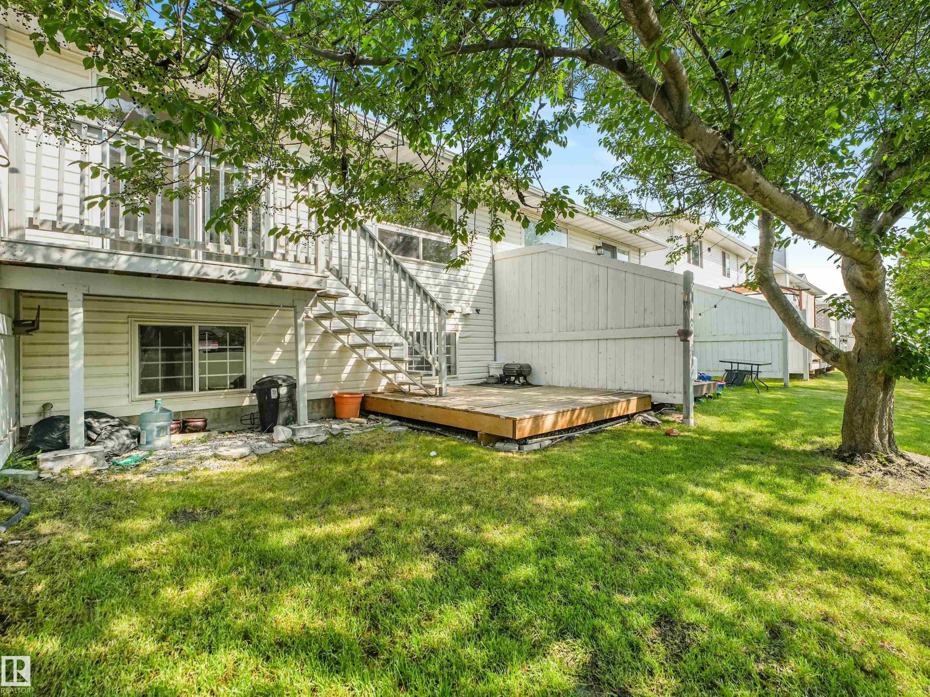 Grassy backyard featuring a wood deck, mature shade tree, and privacy fencing - #2 3311 58 St Nw, Edmonton, AB - Outdoor
