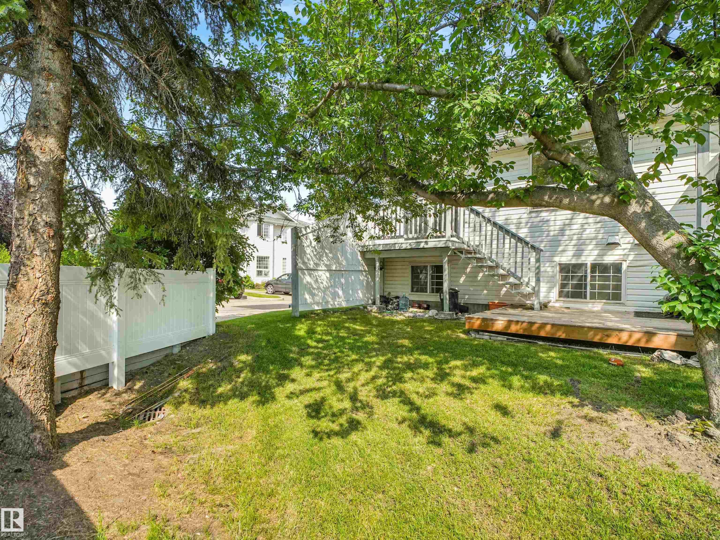 Expansive rear lawn featuring mature trees, a wooden deck, and a white privacy fence - #2 3311 58 St Nw, Edmonton, AB - Outdoor