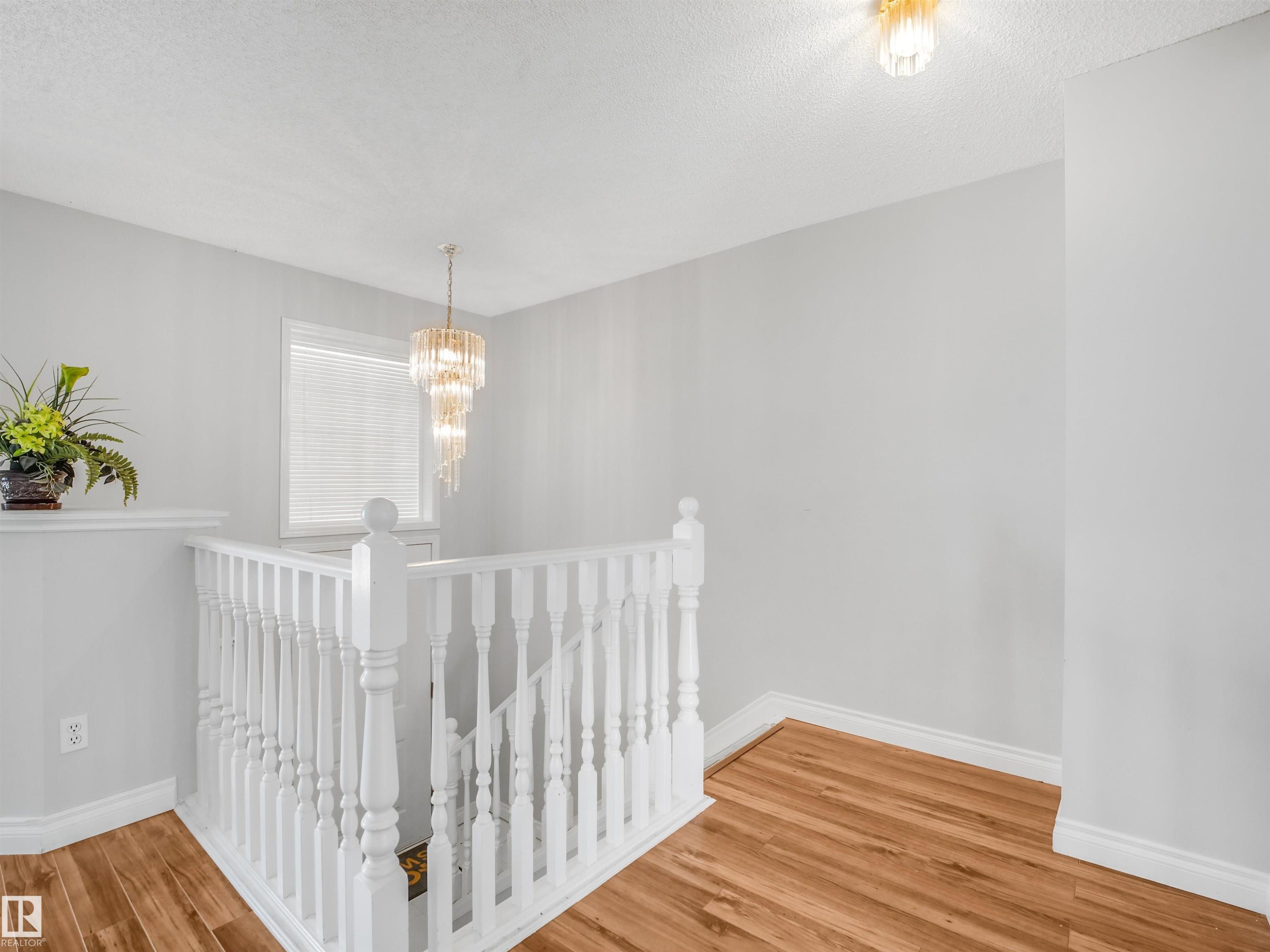 Upper landing featuring wood-finish flooring, white spindle railings, and a tiered crystal chandelier - #2 3311 58 St Nw, Edmonton, AB - Indoor Photo Showing Other Room