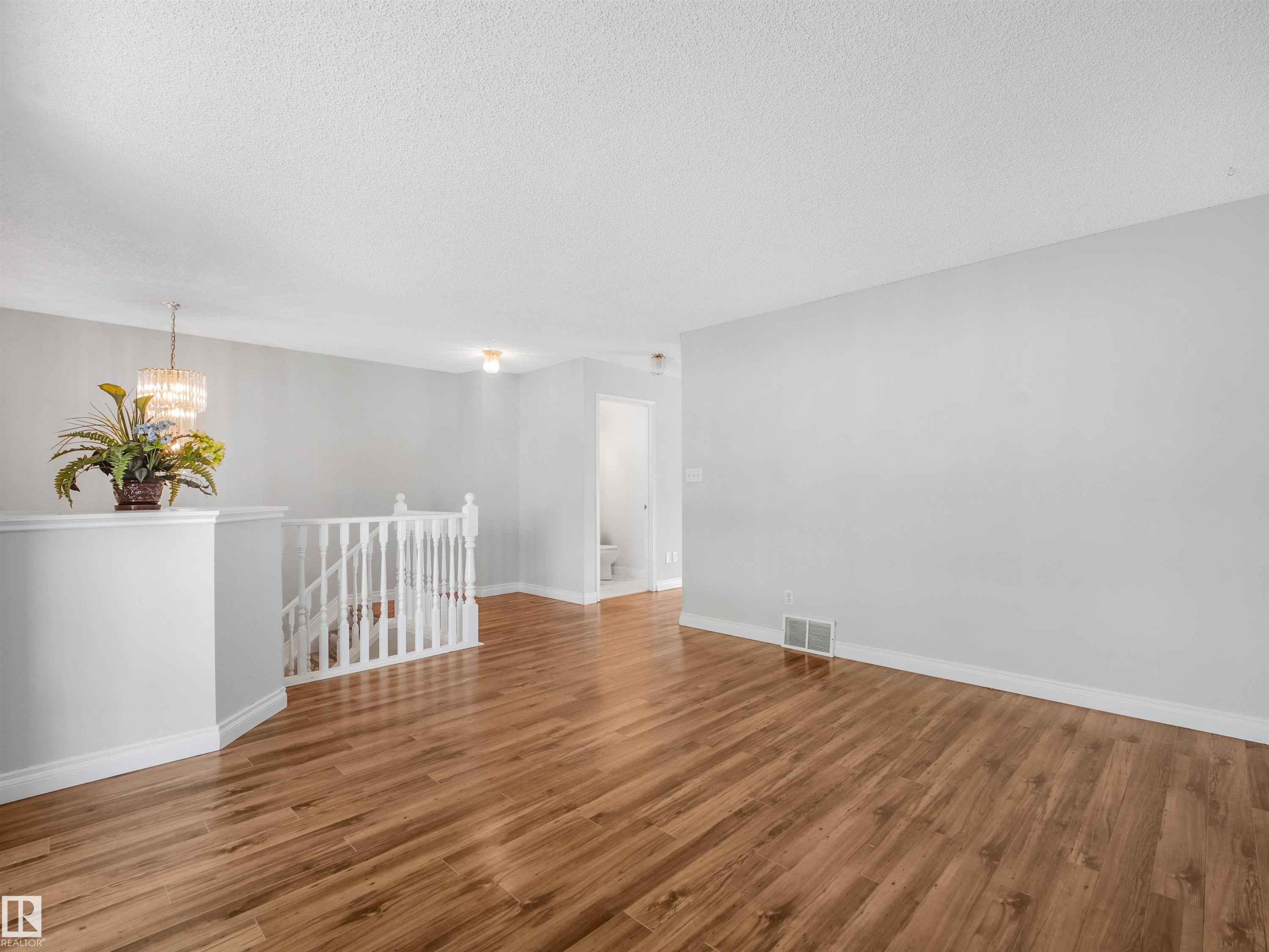 Open living space featuring wood-finish flooring, light grey wall paint, white baseboards, and a white staircase railing - #2 3311 58 St Nw, Edmonton, AB - Indoor Photo Showing Other Room