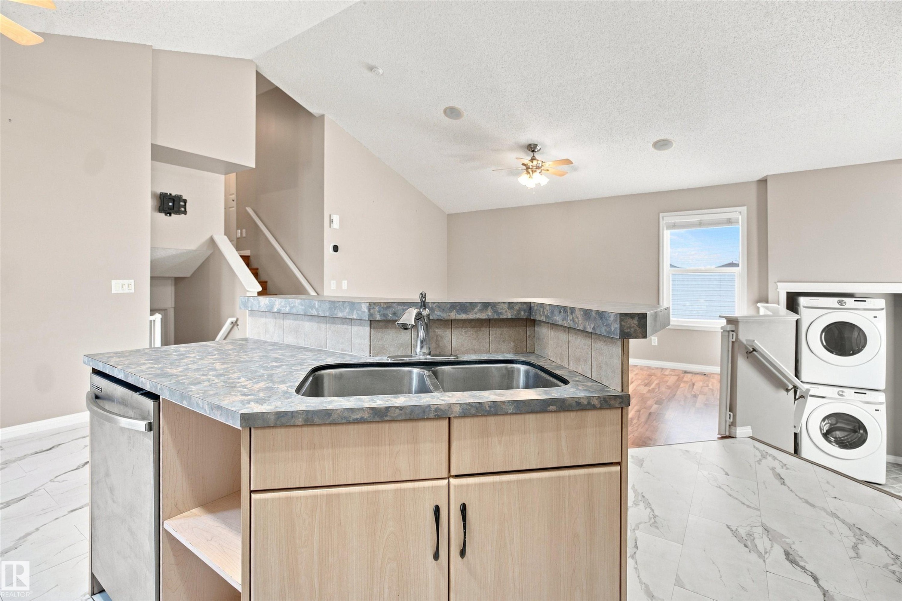 Kitchen island with a double stainless steel sink, integrated dishwasher, and light wood cabinetry - 1328 80 Street Sw, Edmonton, AB - Indoor Photo Showing Laundry Room