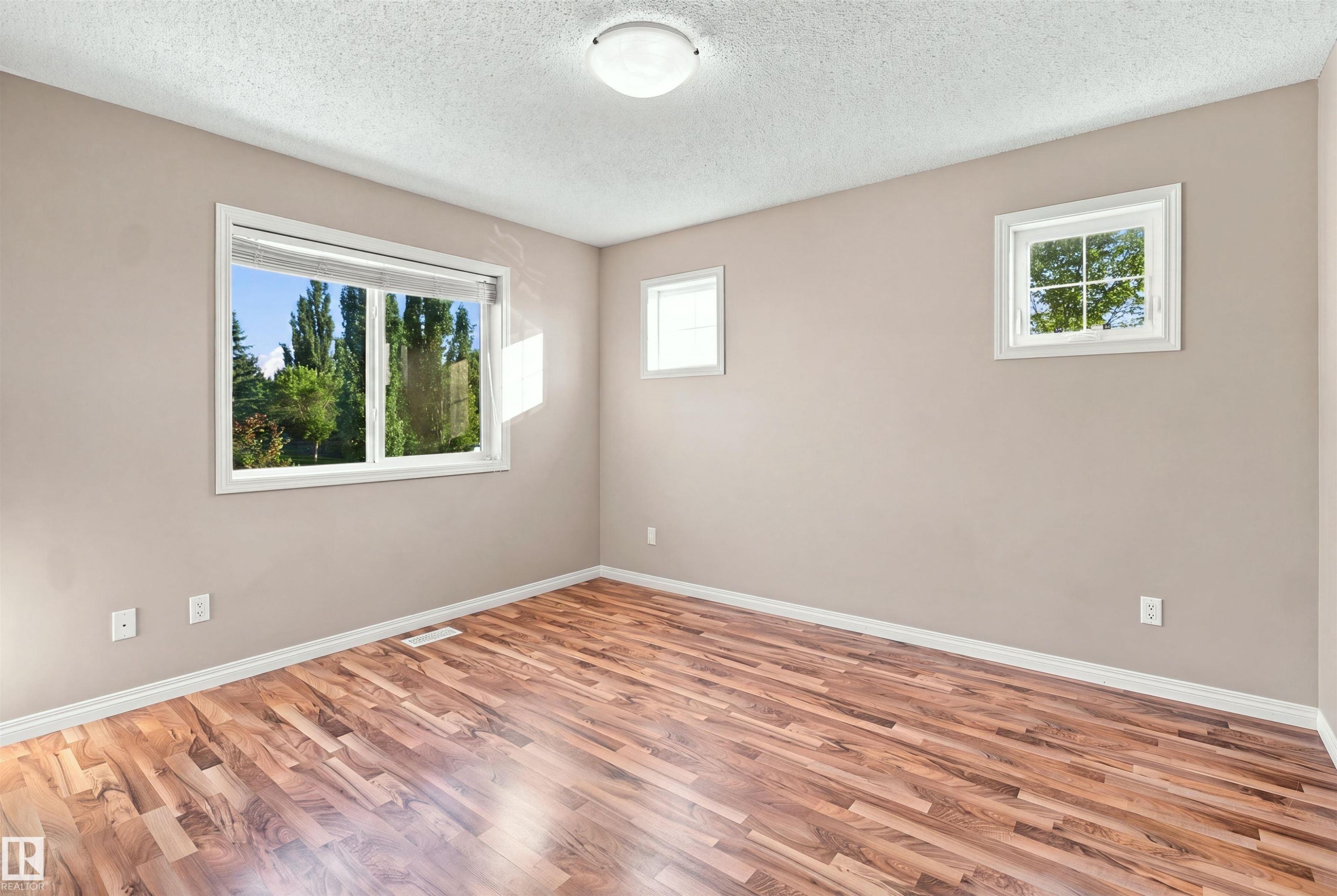Bright room featuring wood-finish flooring, light tan walls, white trim, and a flush mount ceiling light - 1328 80 Street Sw, Edmonton, AB - Indoor Photo Showing Other Room