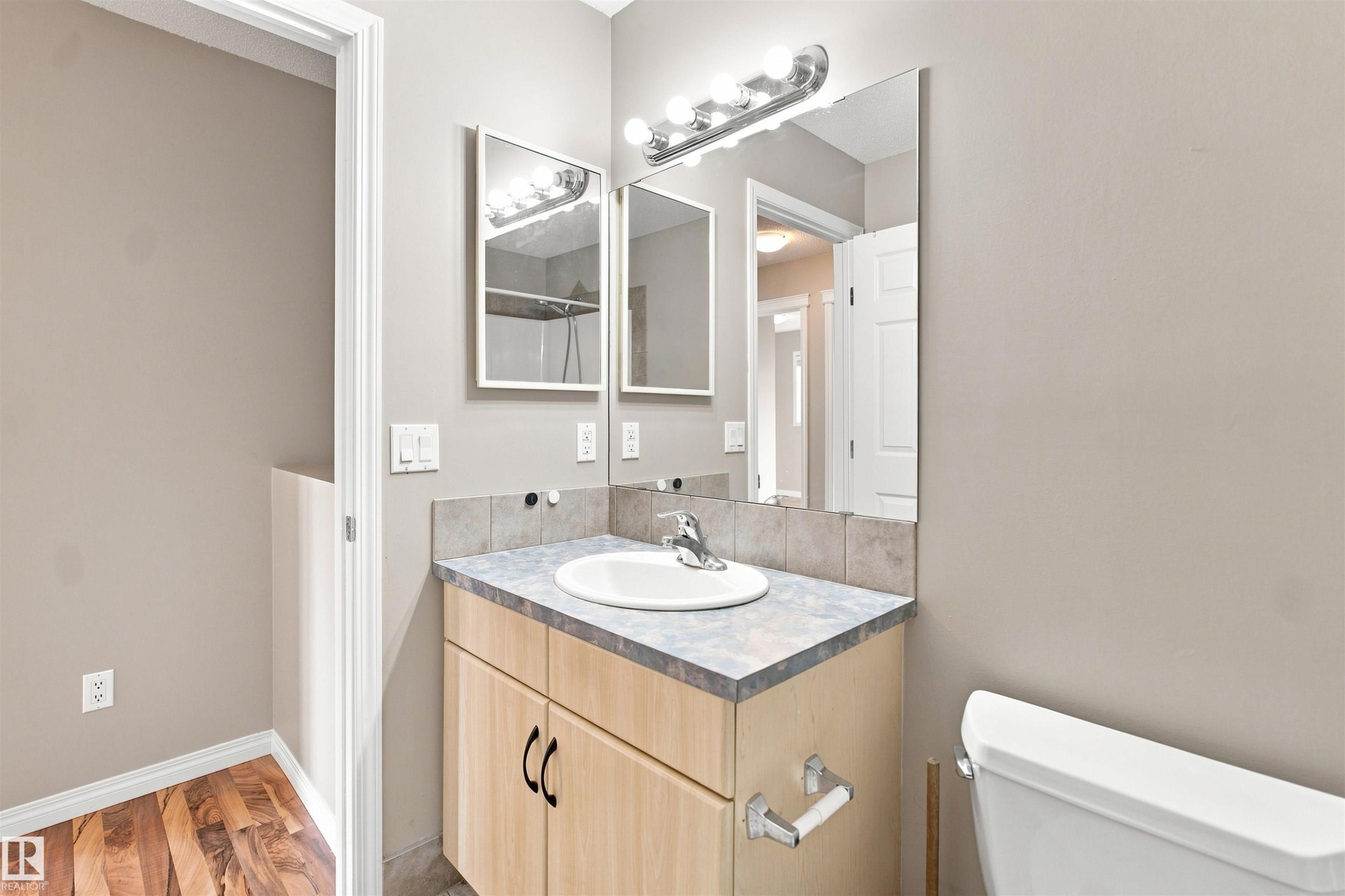 Bathroom vanity featuring a light wood-finish cabinet with black hardware, a laminate countertop, and an integrated white basin - 1328 80 Street Sw, Edmonton, AB - Indoor Photo Showing Bathroom