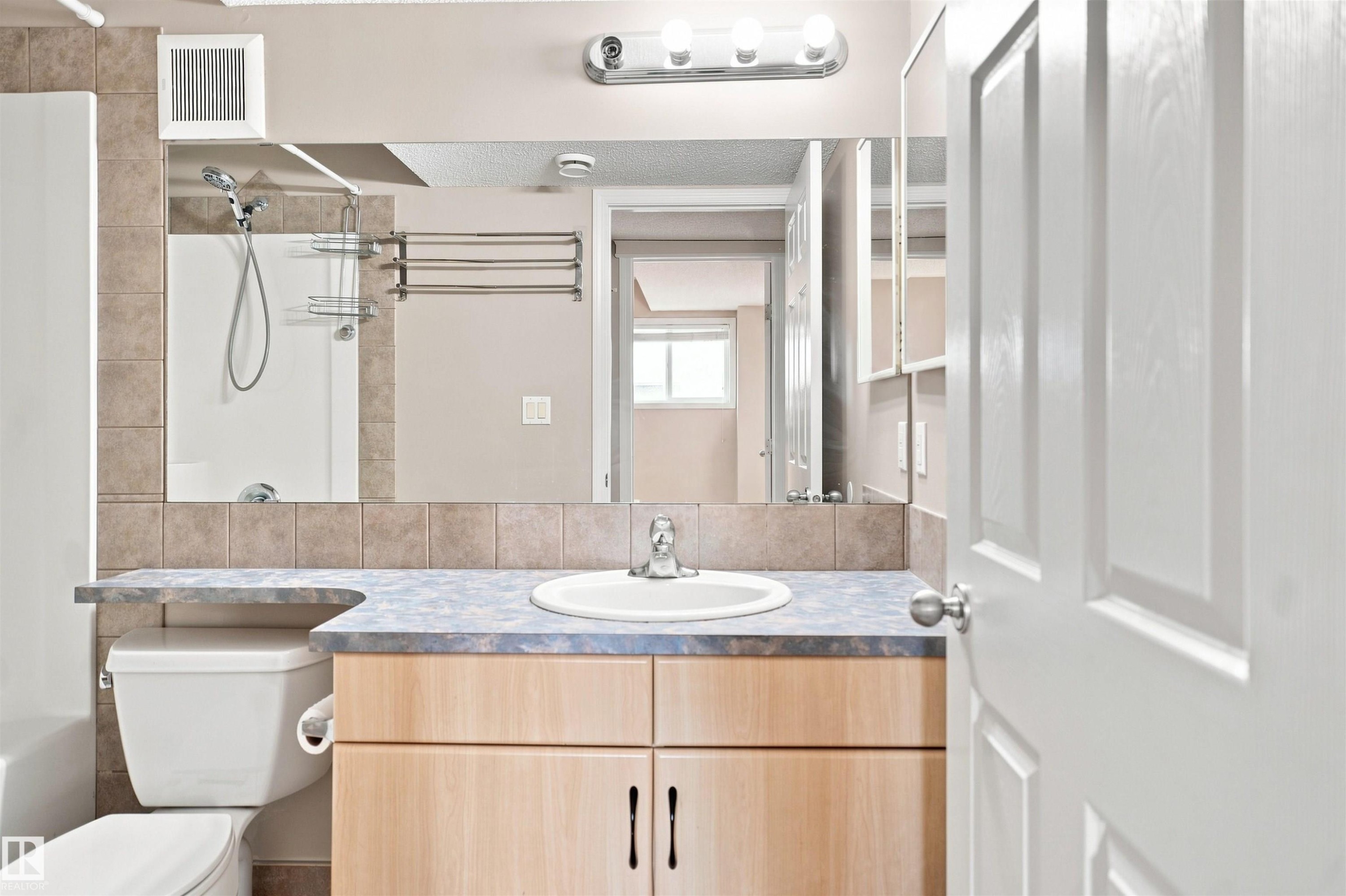 Bathroom featuring a light wood-finish vanity with a blue-hued countertop, an integrated sink, and a wall-mounted mirror - 1328 80 Street Sw, Edmonton, AB - Indoor Photo Showing Bathroom