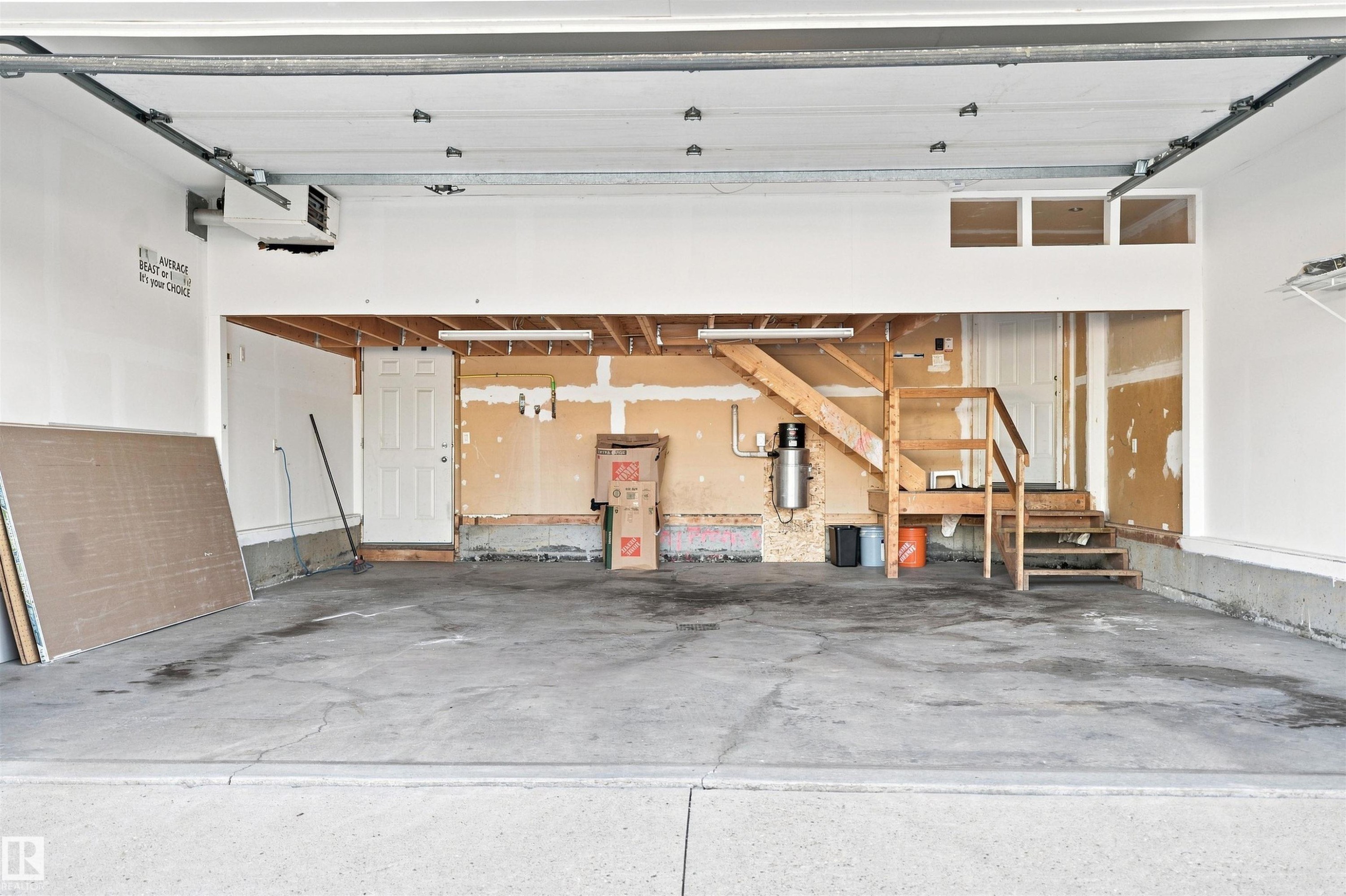 Spacious garage interior featuring concrete flooring, a white overhead garage door mechanism, an interior doorway, and unfinished framing with an exposed staircase - 1328 80 Street Sw, Edmonton, AB - Indoor Photo Showing Garage